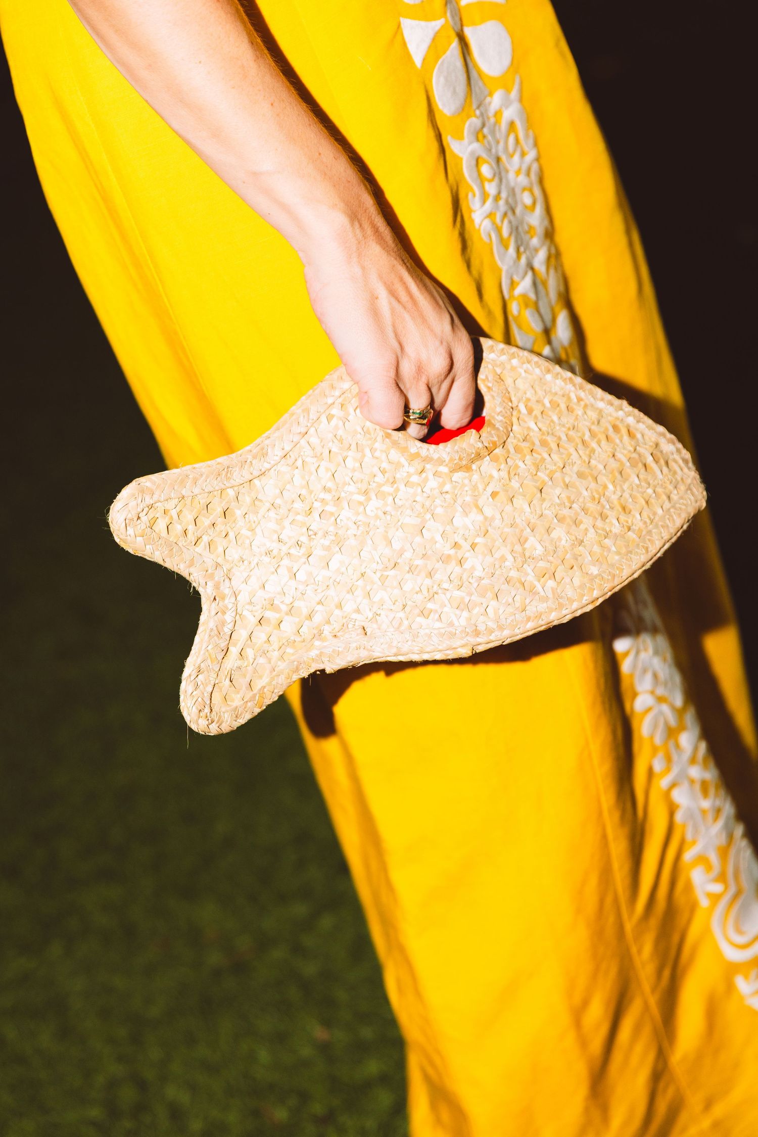Person in yellow embroidered maxi dress holding a fish-shaped woven straw clutch bag.