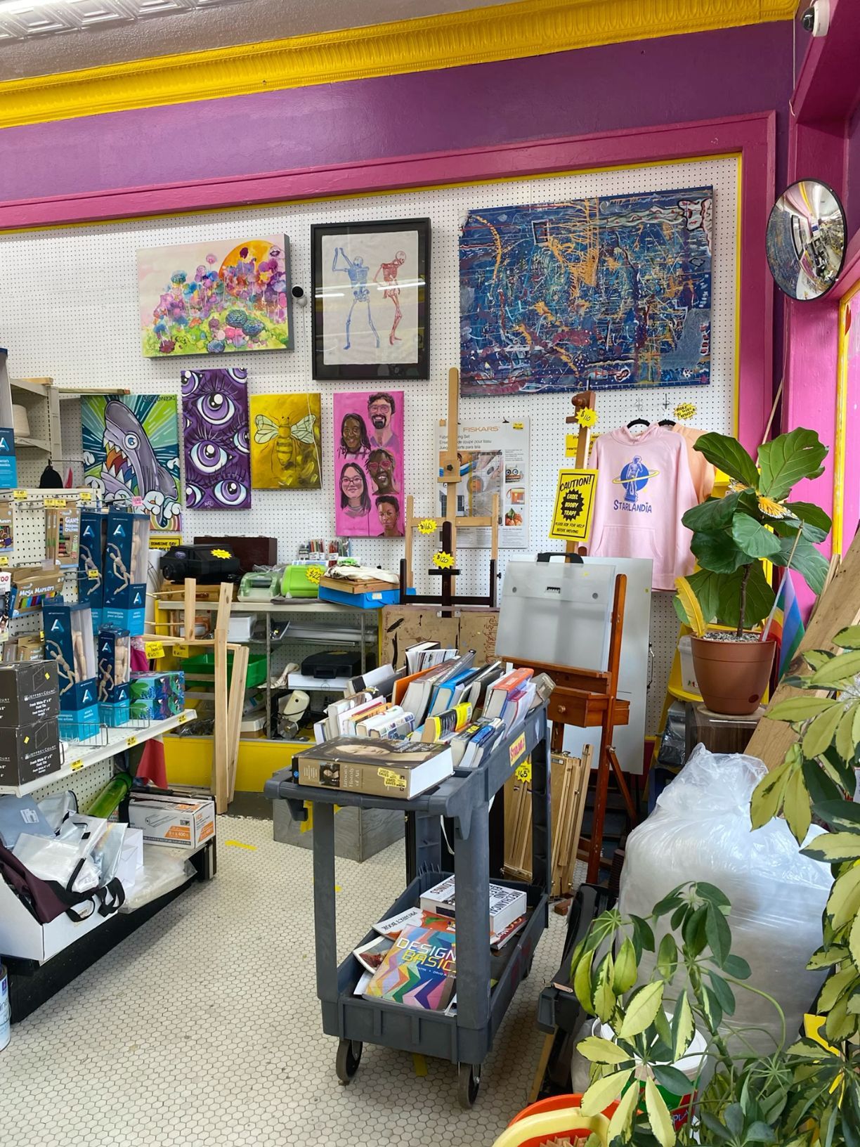 Colorful art supply and gift shop interior with eclectic artwork, merchandise displays, and bright pink walls.