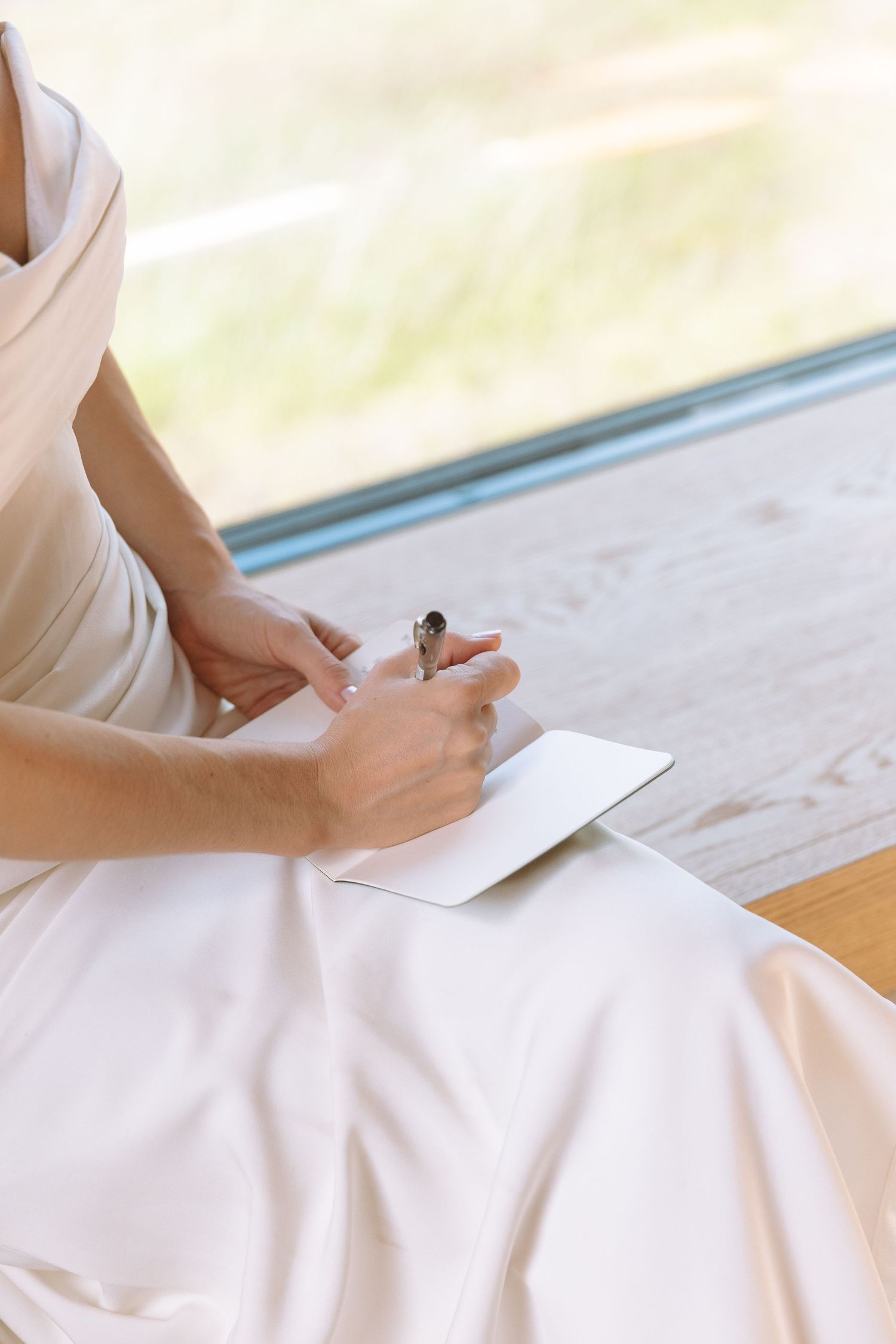 Close-up of a bride in white writing vows in a small notebook, wearing a diamond ring.