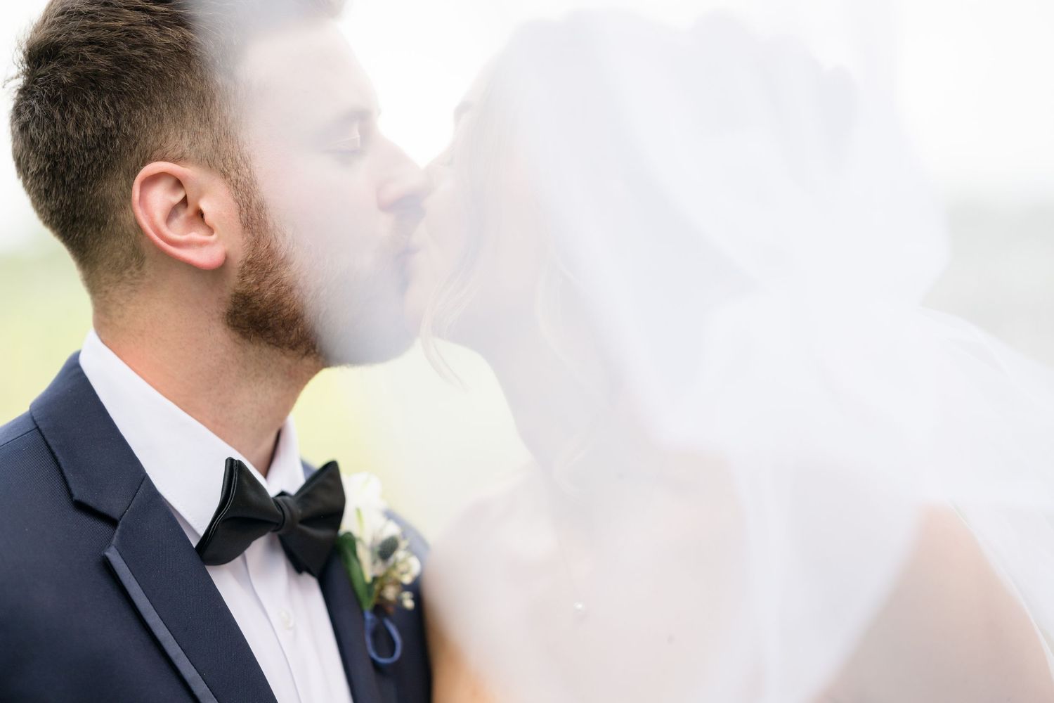 Formal wedding attire details with bow tie and boutonniere against white background.