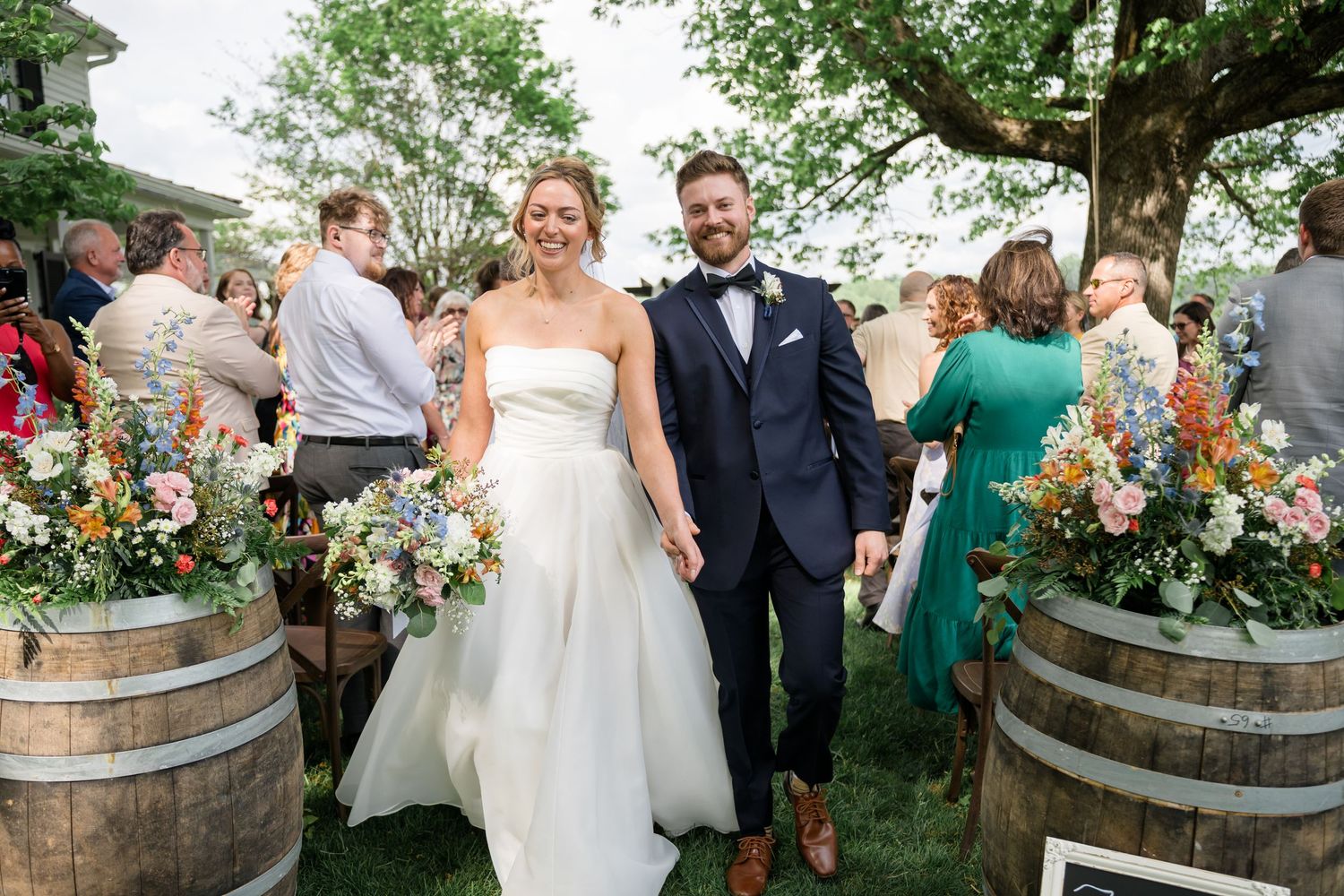 Wedding reception gathering with rustic barrel decor and floral arrangements outdoors.