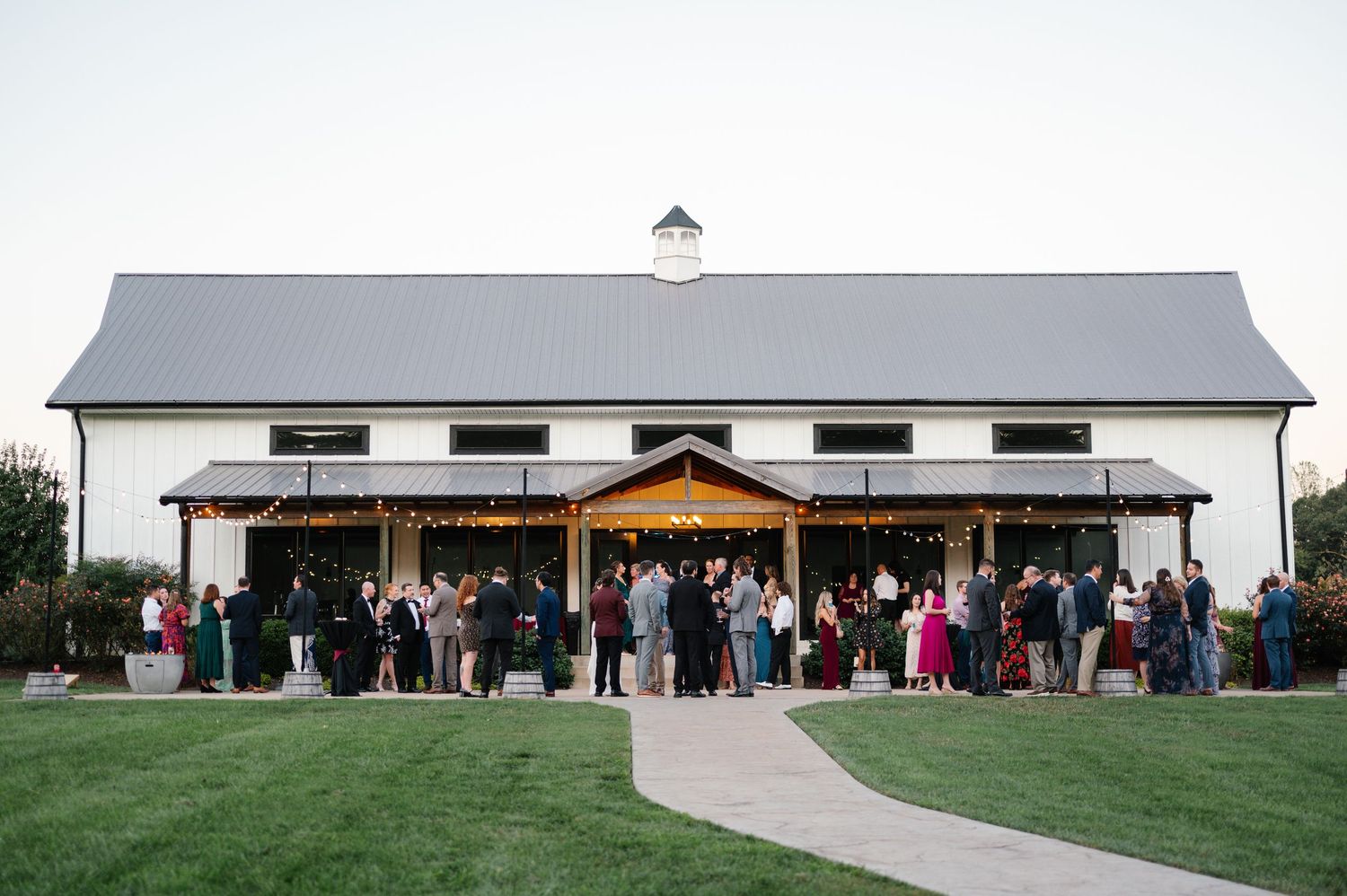 Panoramic view of wedding guests gathered outside modern white barn venue.