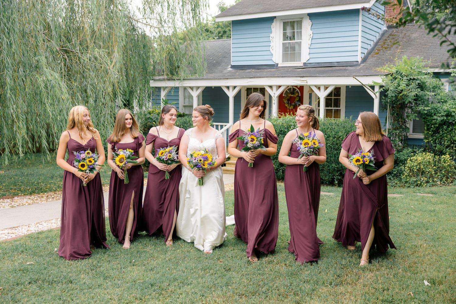 Wedding party in burgundy dresses posing under a willow tree.