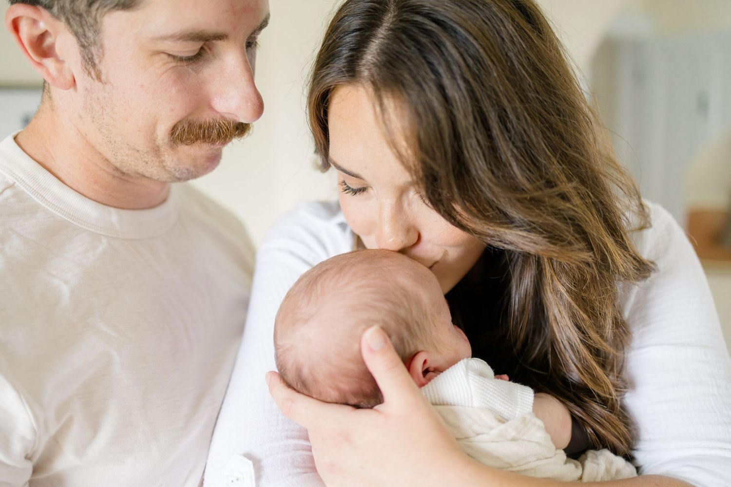 Tender family moments captured in bright white room with natural window light.