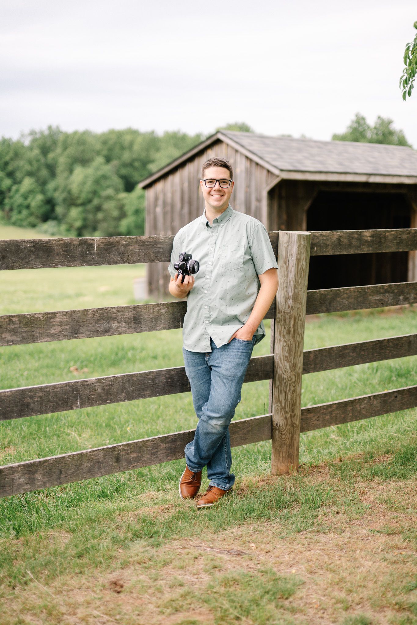Casual portrait session by rustic wooden fence in countryside setting.