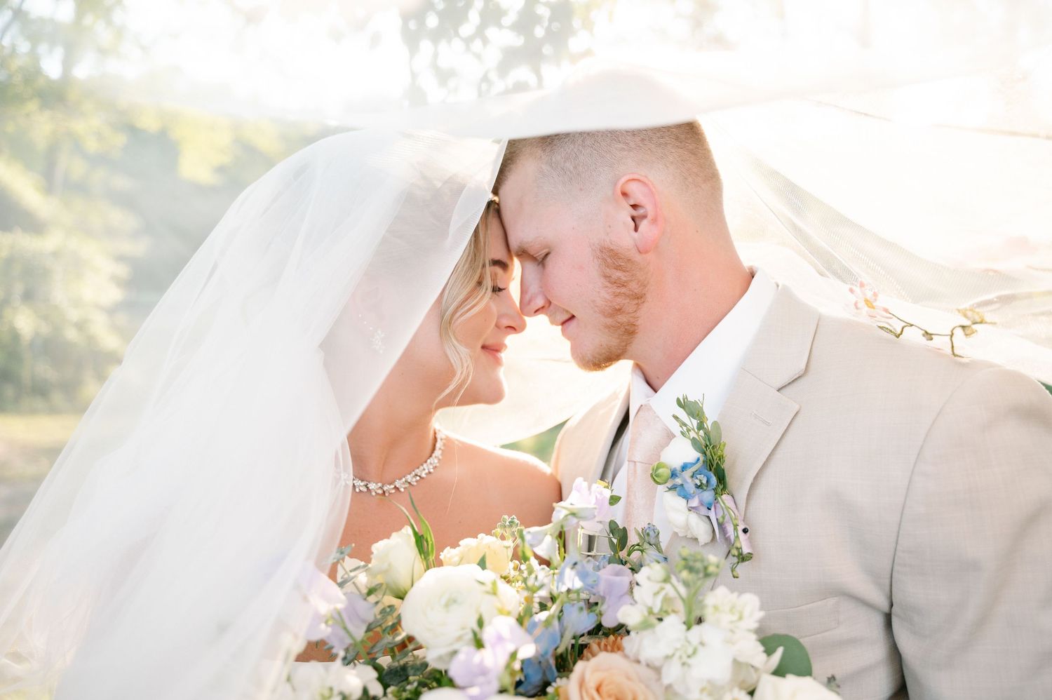 Romantic wedding portrait with couple sharing intimate moment under flowing veil.
