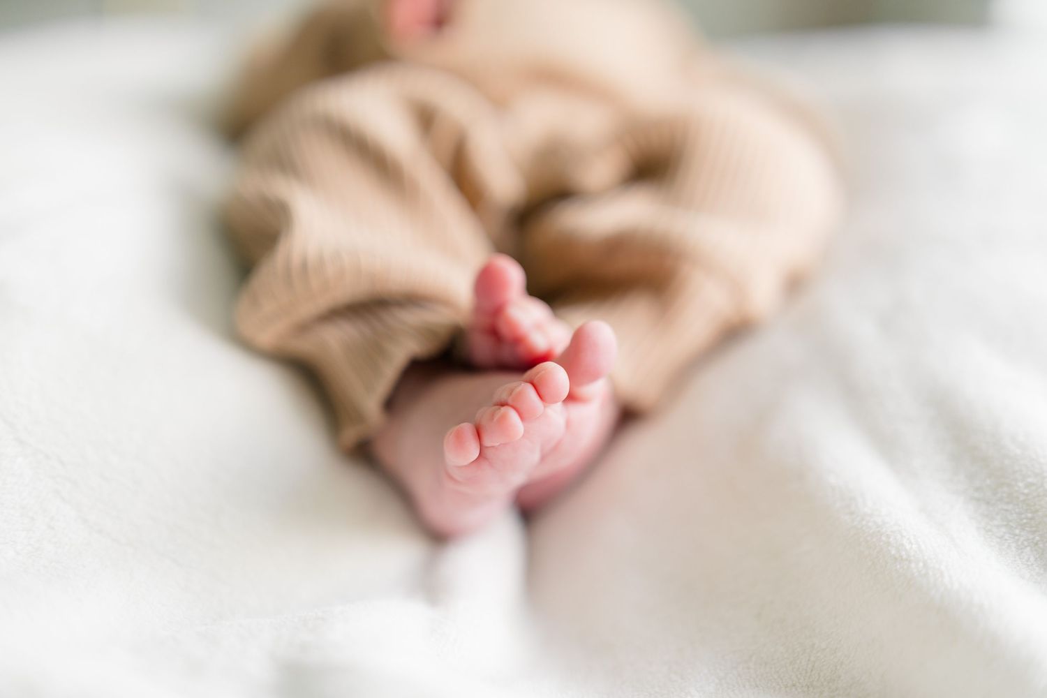 Close-up detail shots of newborn baby's tiny feet on white bedding.