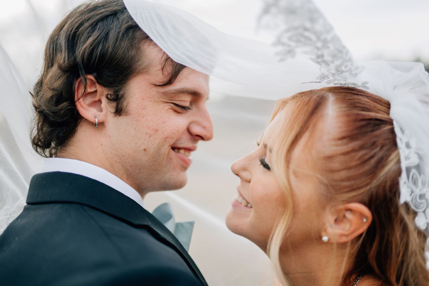 Close-up romantic moment between newlyweds under a white veil.