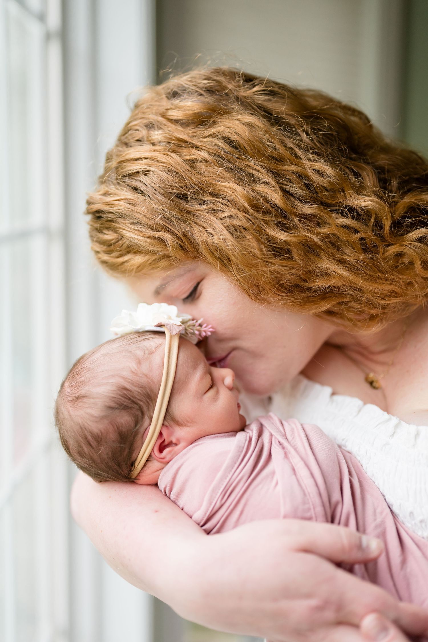Tender moment between parent and baby in soft natural window light.