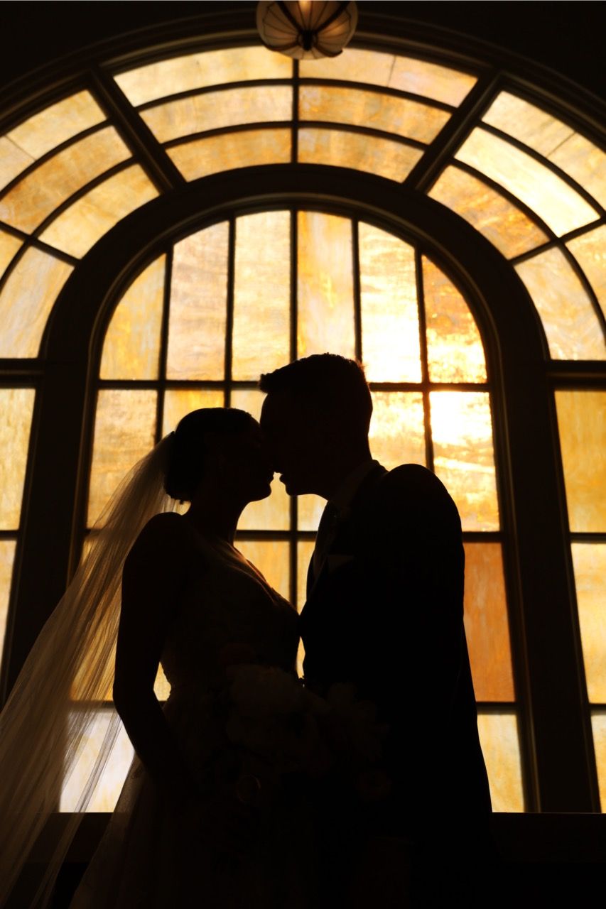 Silhouetted bride and groom against golden arched windows