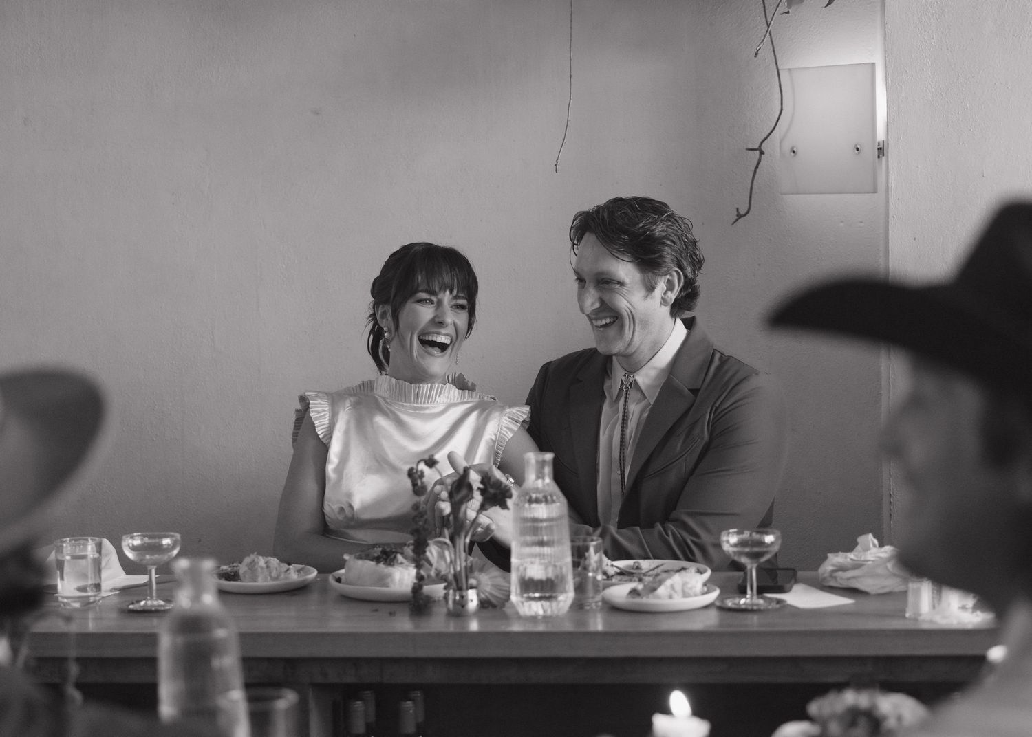 Black and white photo of a laughing bride and groom seated at a dinner table during their wedding reception.