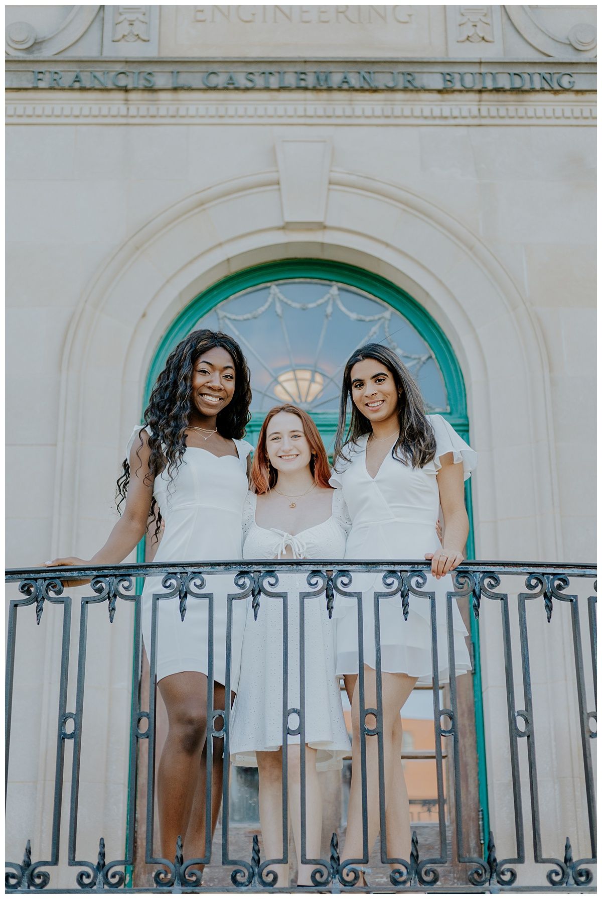 Friends in white dresses stand together on a balcony of the Francis Castleman Jr Building.