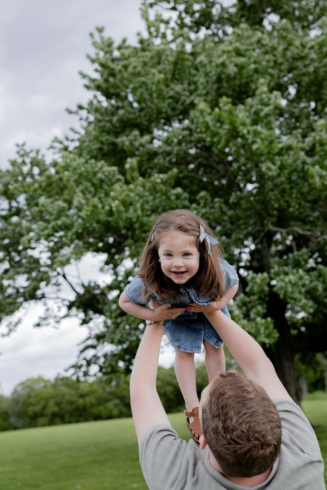 A joyful moment captured as a child is lifted high in the air against a backdrop of green trees.