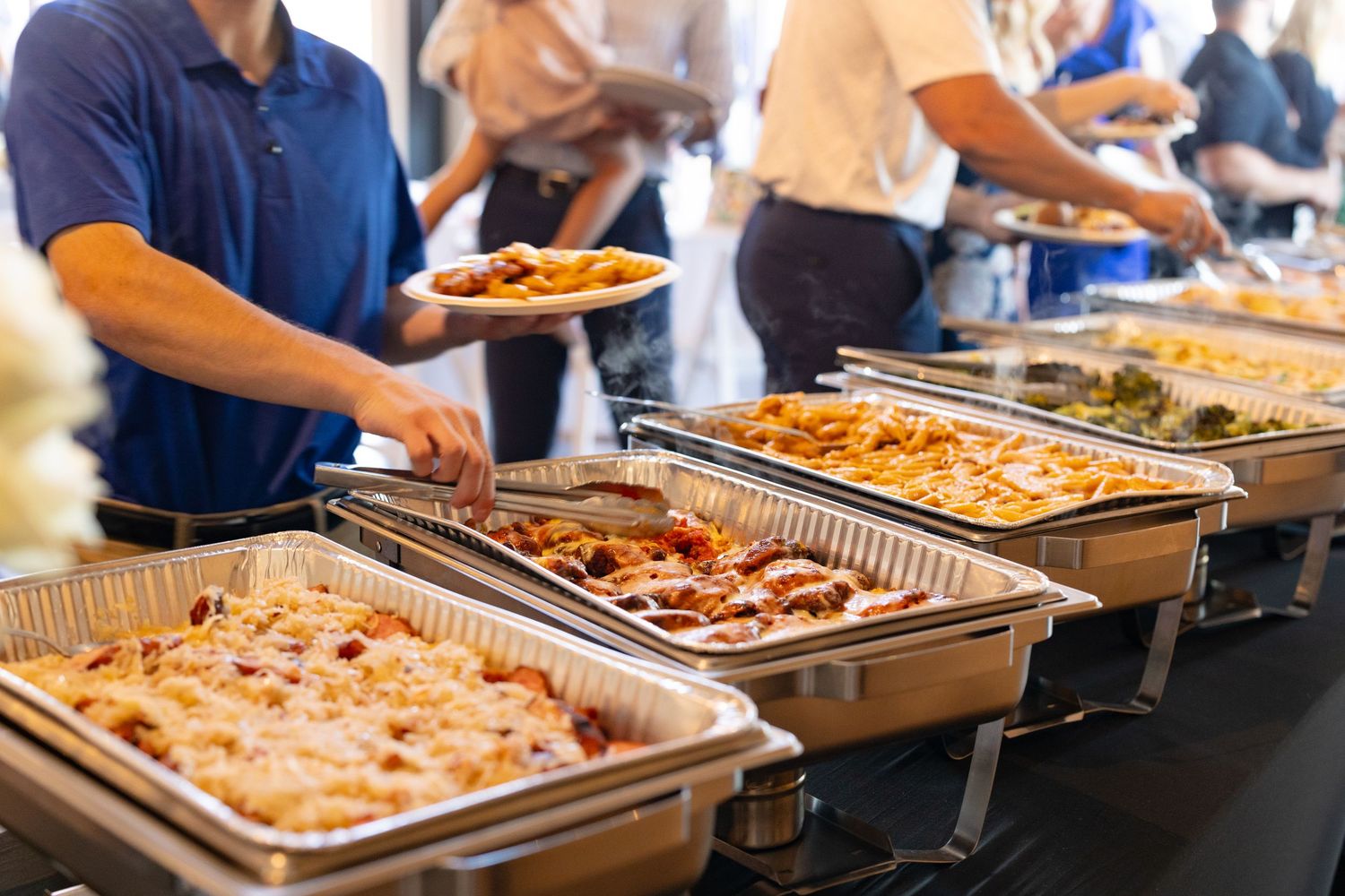 A buffet line of catering trays with various dishes at an event.
