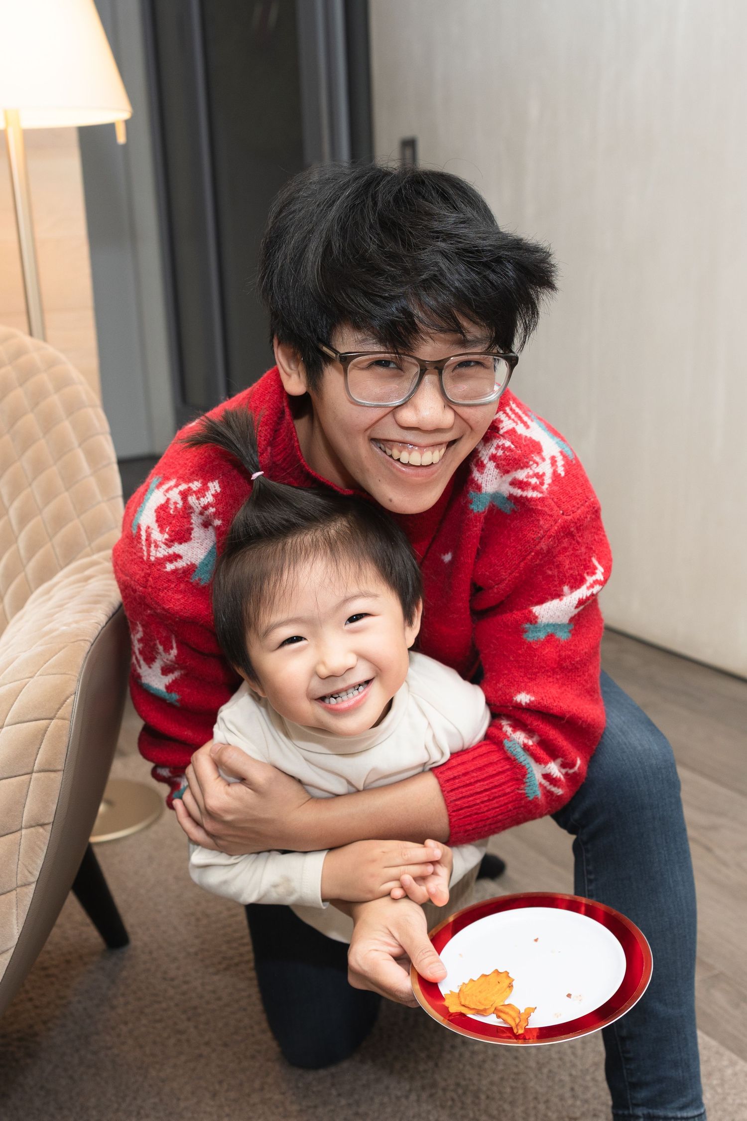 Two people share a joyful moment while wearing festive holiday sweaters, with a red plate nearby.