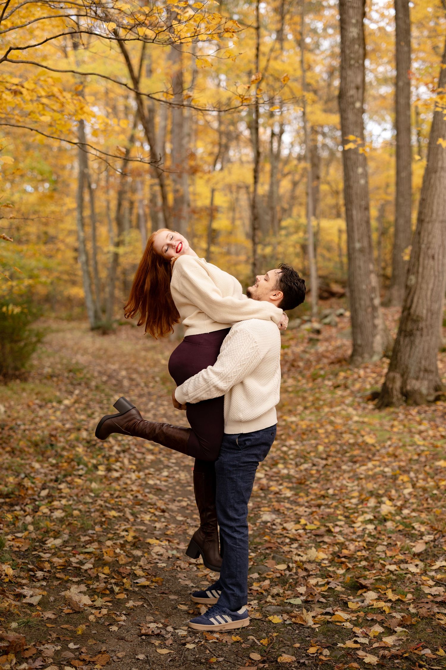 A couple embraces in a romantic autumn forest scene with golden yellow foliage and fallen leaves on the ground.