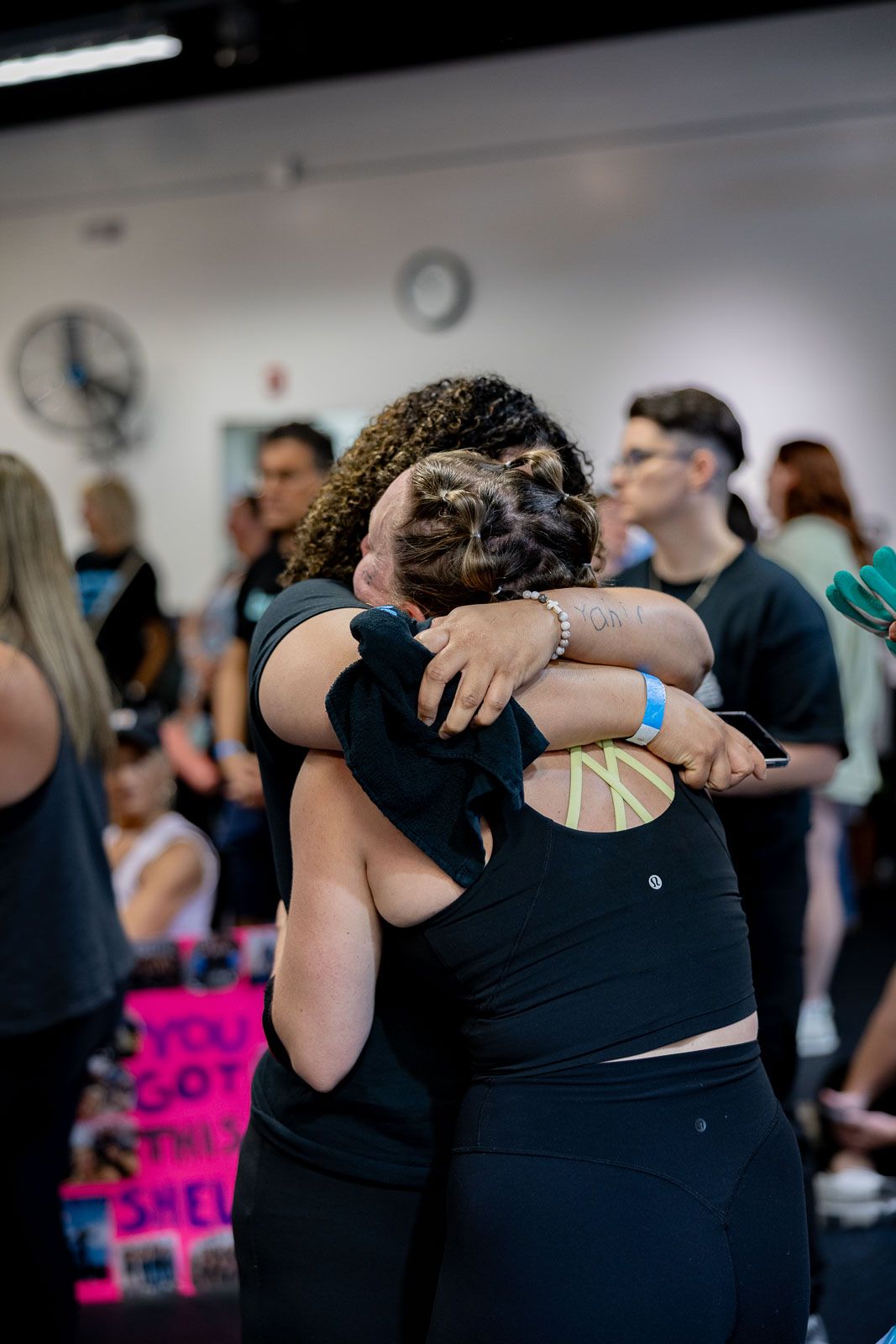 Two people in black attire embrace emotionally during a gathering in an indoor space.