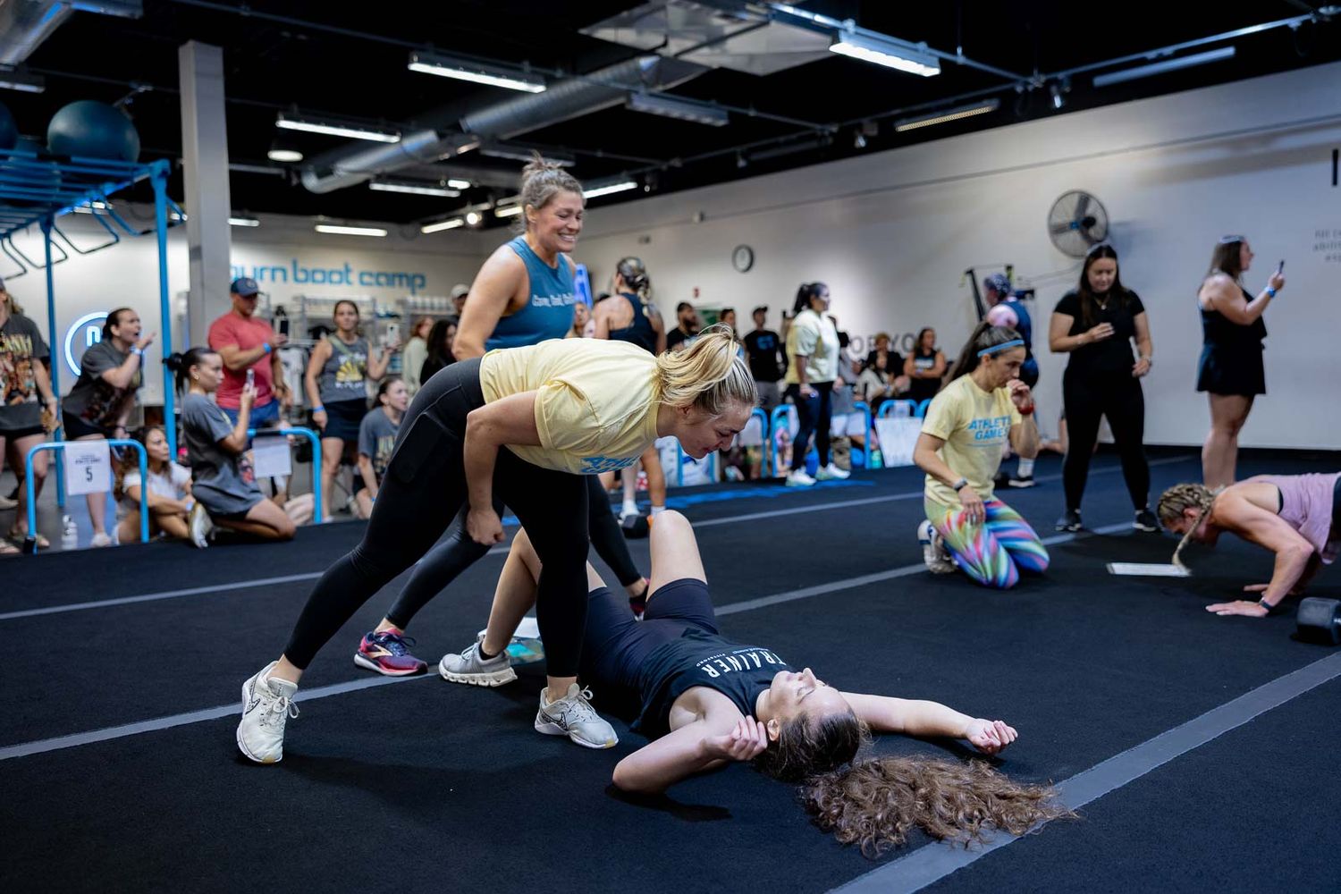 Group workout participants performing floor exercises in a dimly lit gym space with dark flooring.
