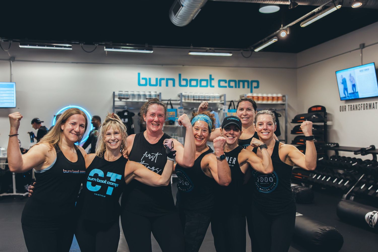 Group of fitness enthusiasts flexing their muscles and posing together at Burn Boot Camp gym.