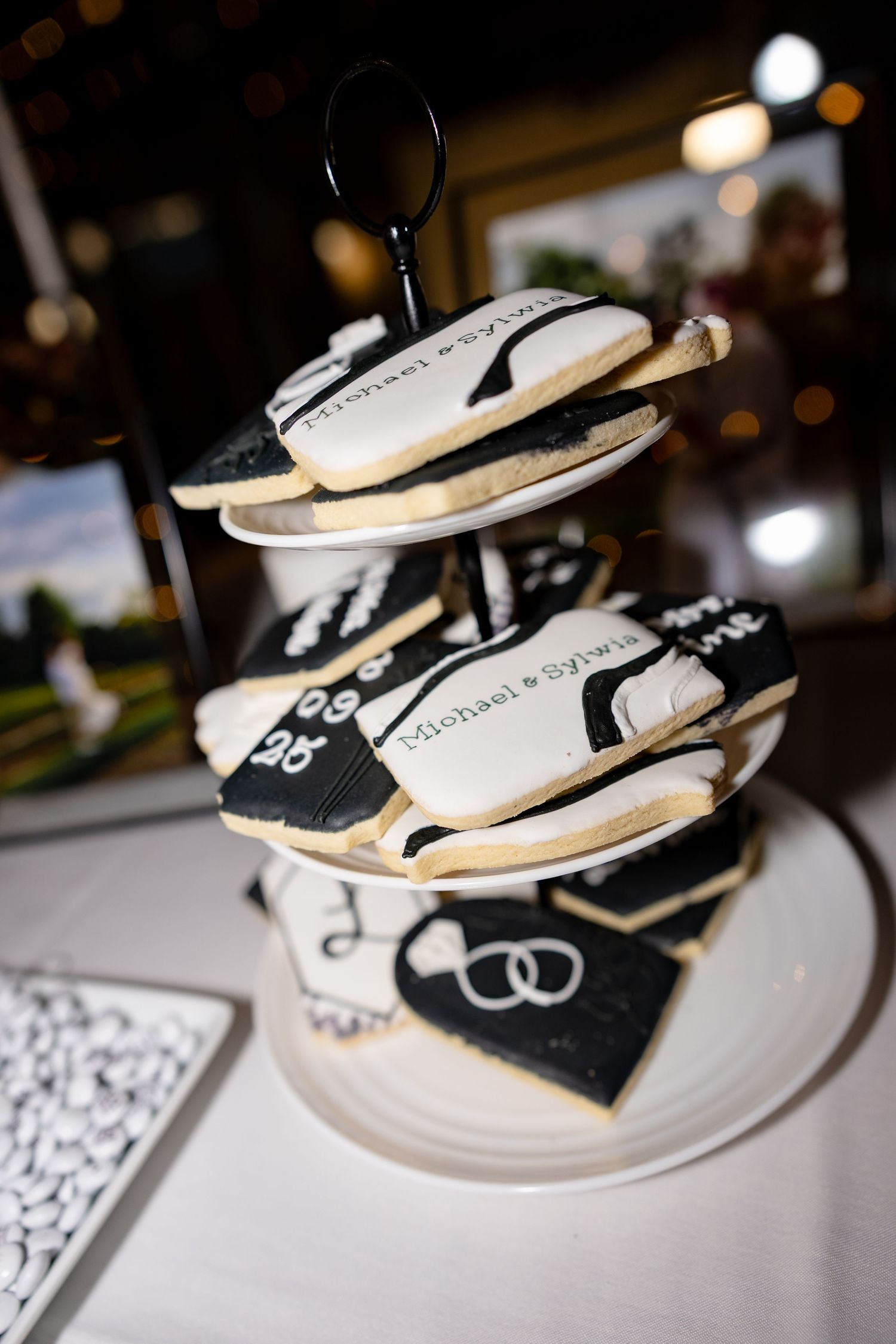 Black and white wedding cookies decorated with rings arranged on tiered plates.