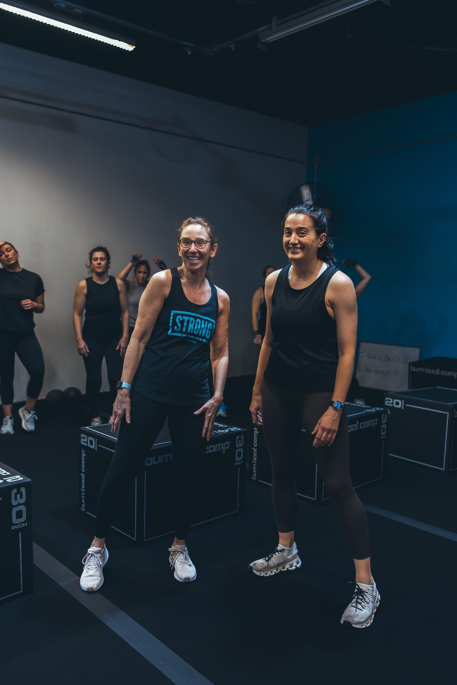 Two people standing on workout platforms during fitness class in dark gym interior.