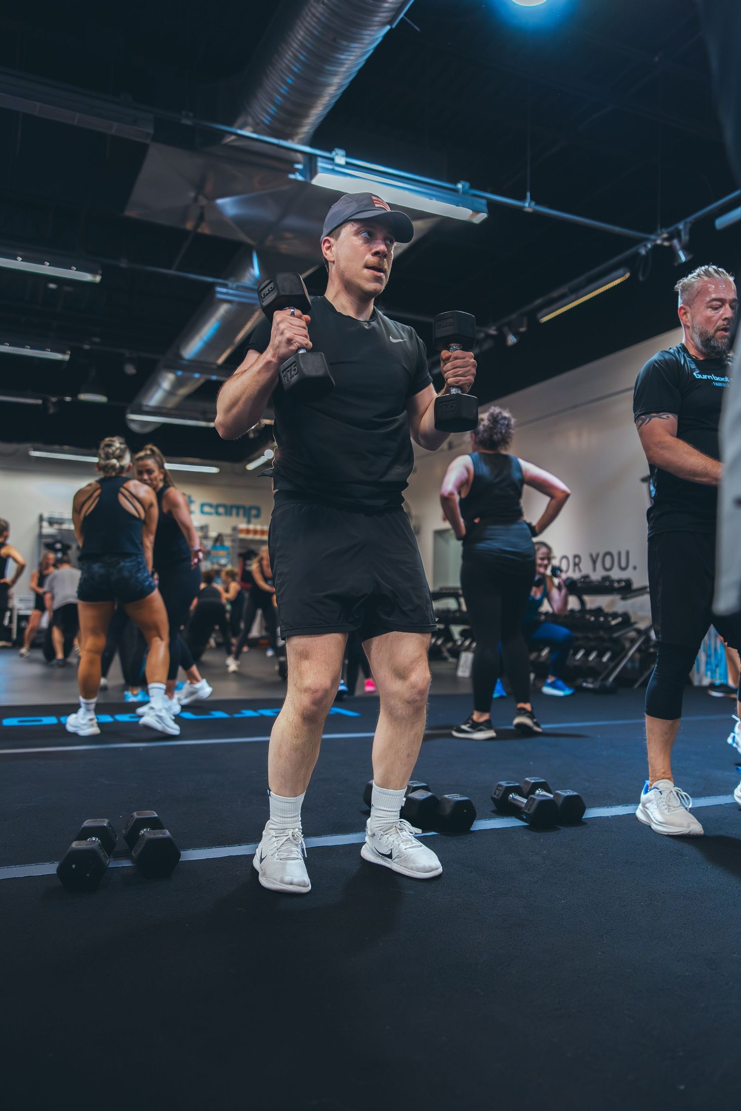 Person in black athletic wear exercising with dumbbells during an indoor fitness class.