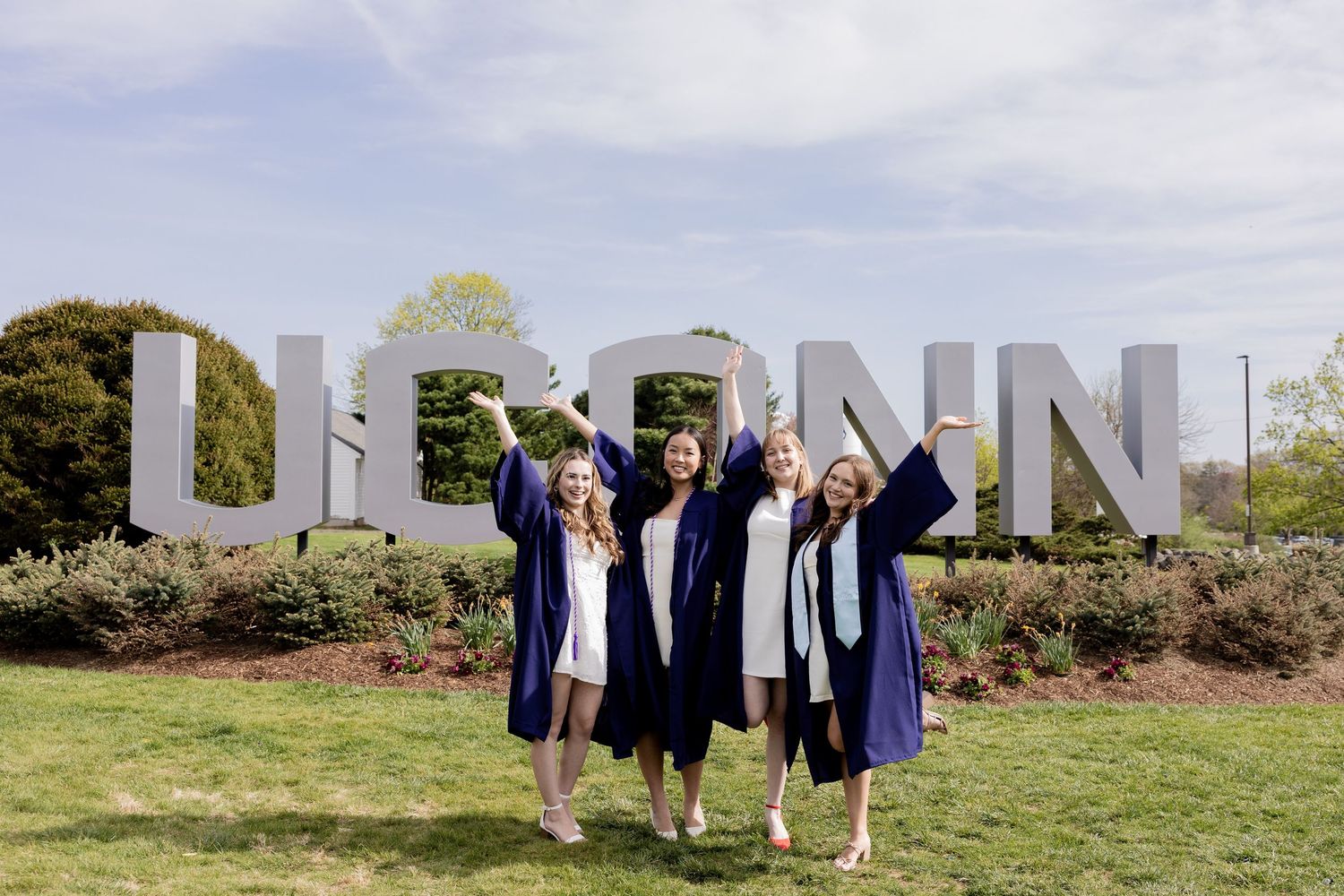 Graduates celebrate in front of large UCONN letters on campus lawn during graduation day.