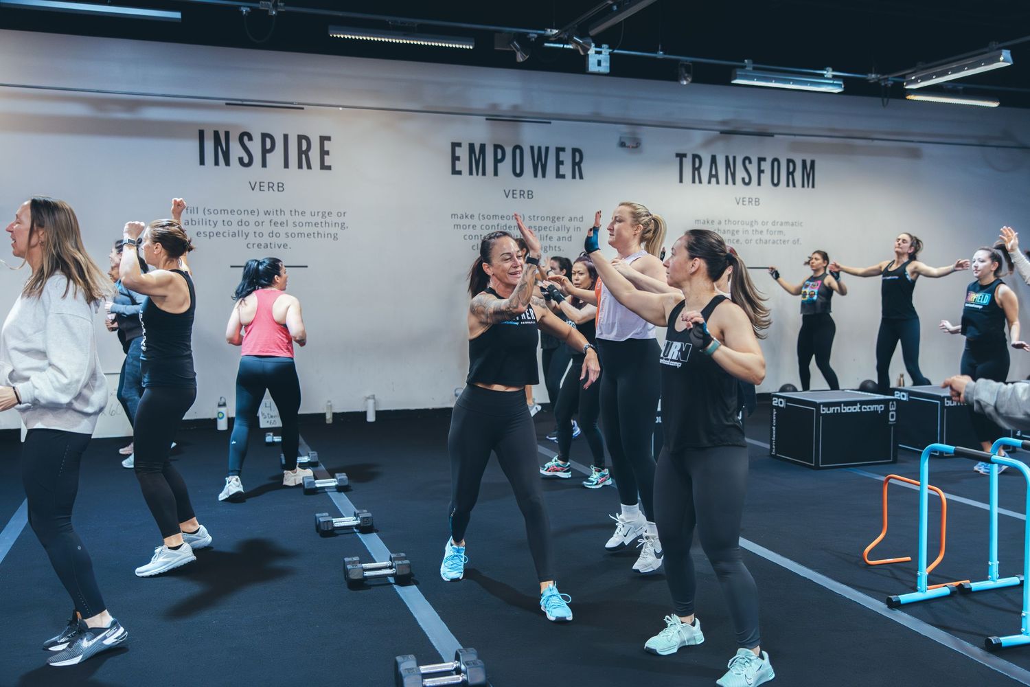 Group fitness class exercising together in modern gym with motivational words on wall.