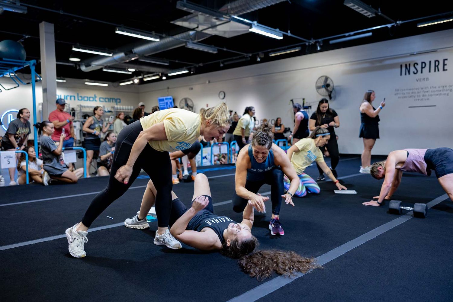 Multiple athletes perform burpee exercises on blue mats during an intense fitness competition.