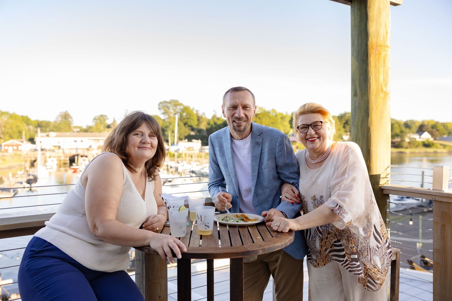 Friends gathering at an outdoor restaurant patio overlooking the water.