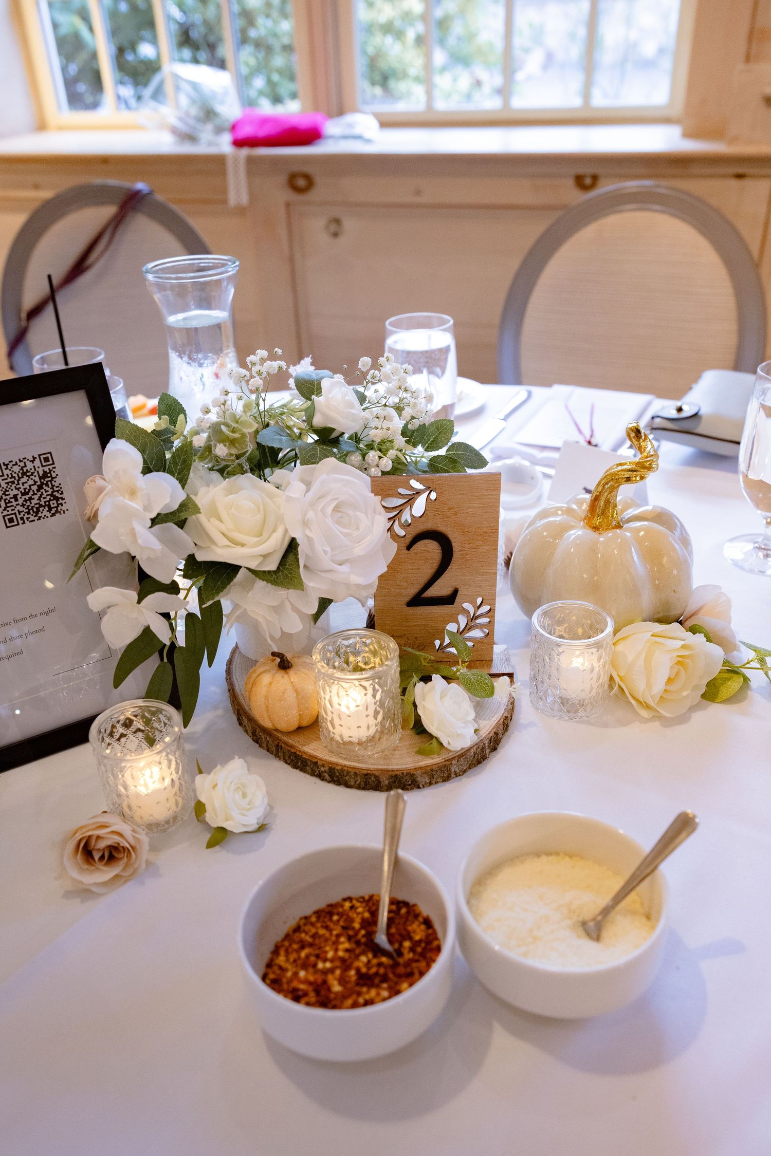 White floral centerpieces with candles and table numbers displayed on wooden chargers at an elegant event setting.