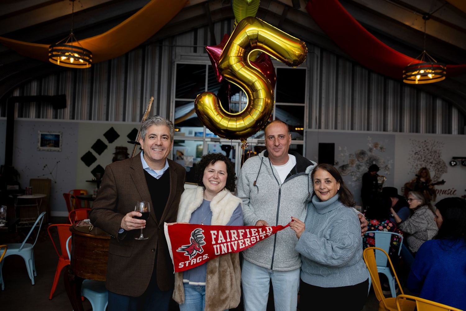 A group celebrating with a large number 5 balloon and a red banner at a festive party.