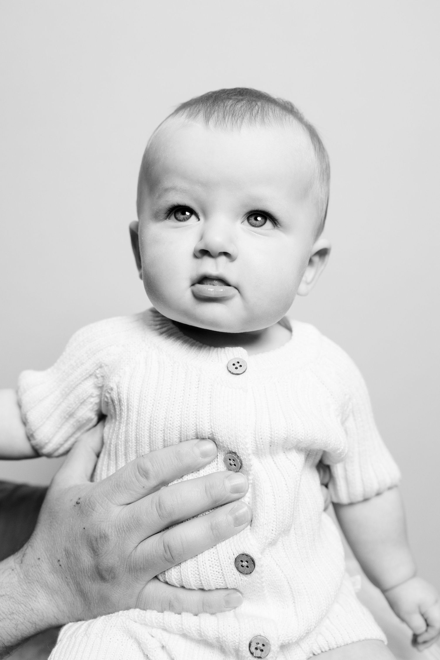 Series of black and white baby portraits showing different angles in a white knit outfit.