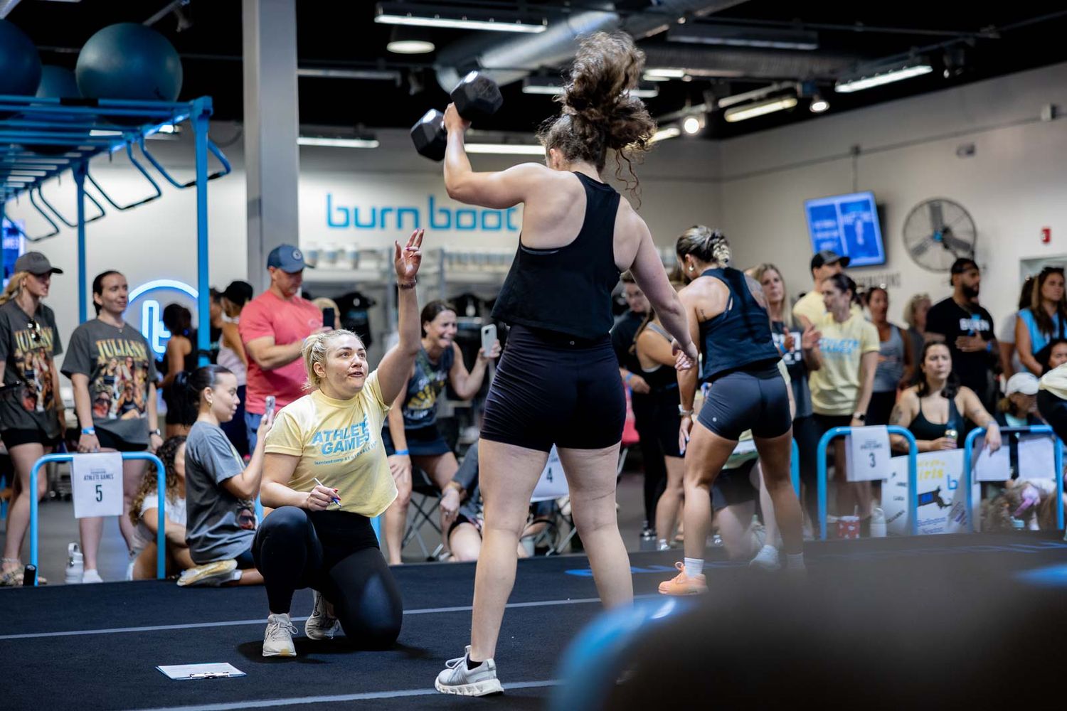 Group fitness class participants do pushups together on blue exercise mats during an indoor workout session.