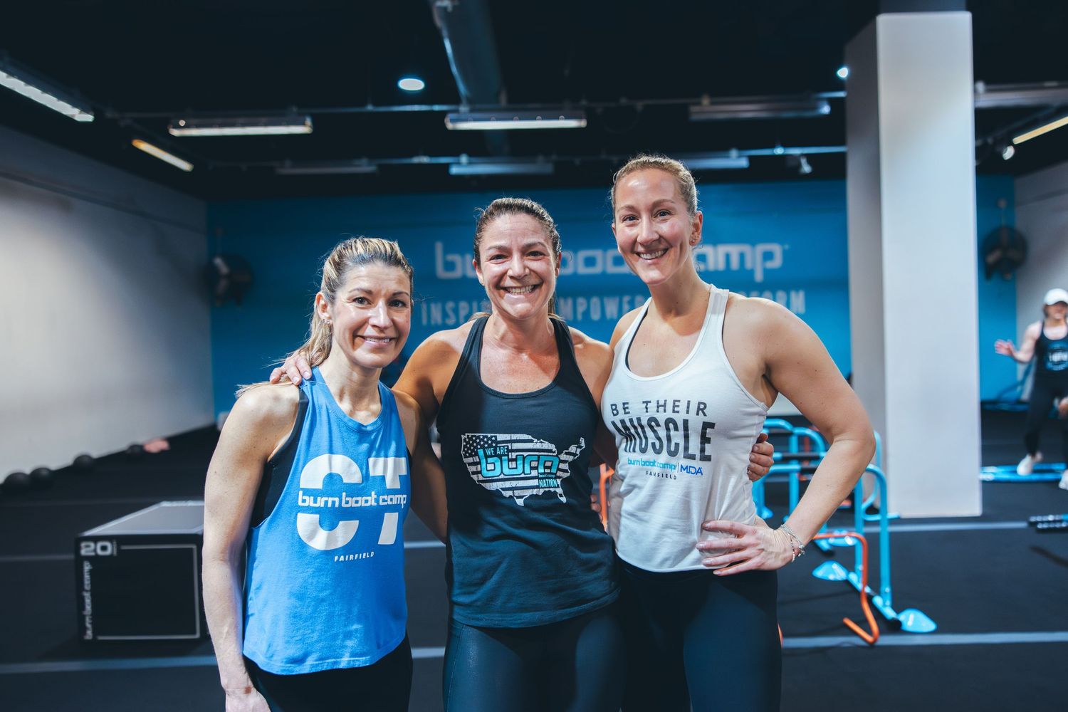 Three athletes in workout attire smiling together after a training session.
