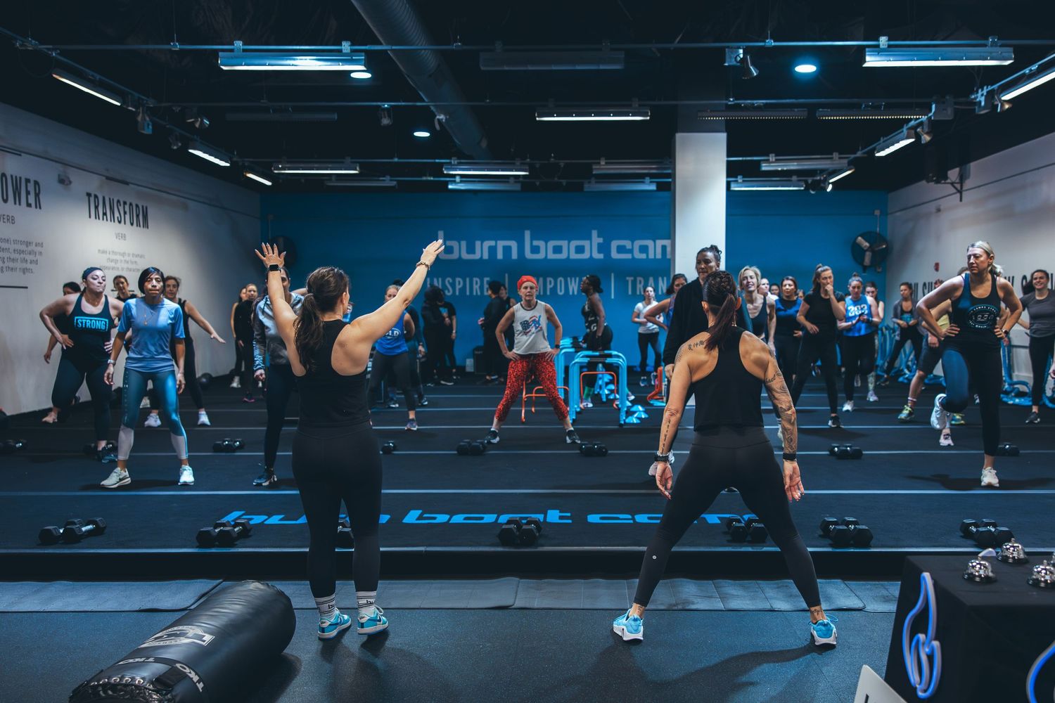 Wide shot of energetic boot camp fitness class in session with multiple participants.