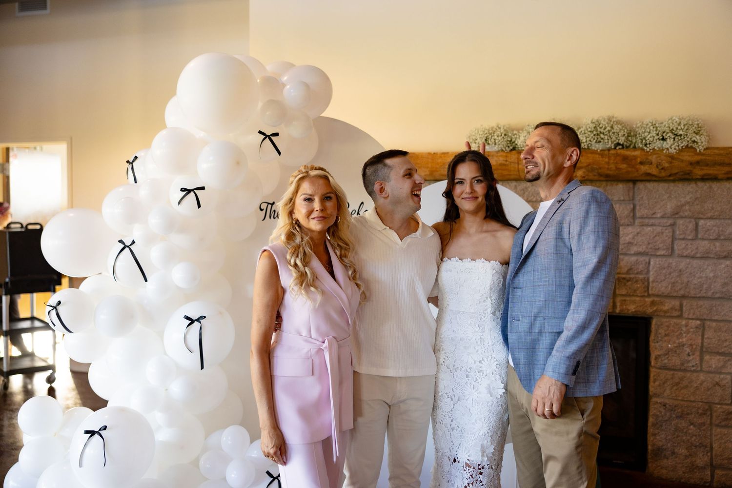 Wedding party members gather for photos in front of a decorative white balloon arch.