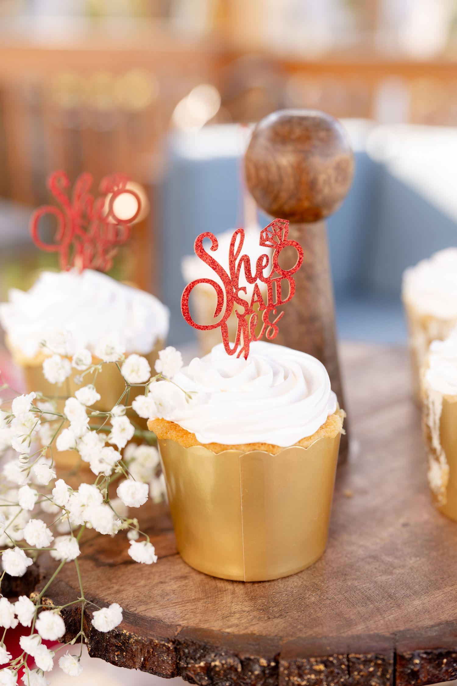 Delicate white baby's breath flowers accent gold dessert stands with whipped cream topped treats on a wooden surface.
