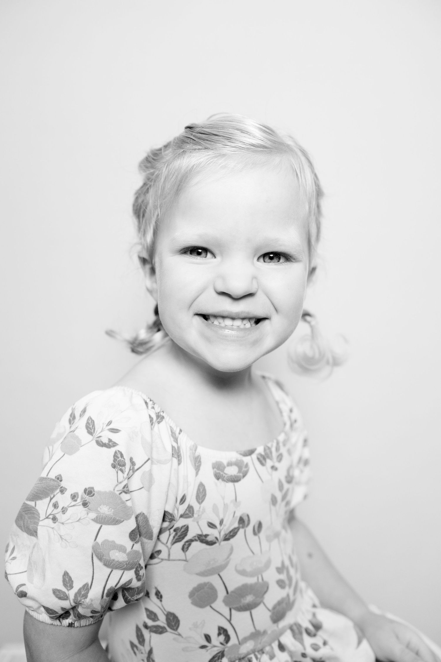 A black and white photo series showing a young child wearing a floral print dress with a bright expression.