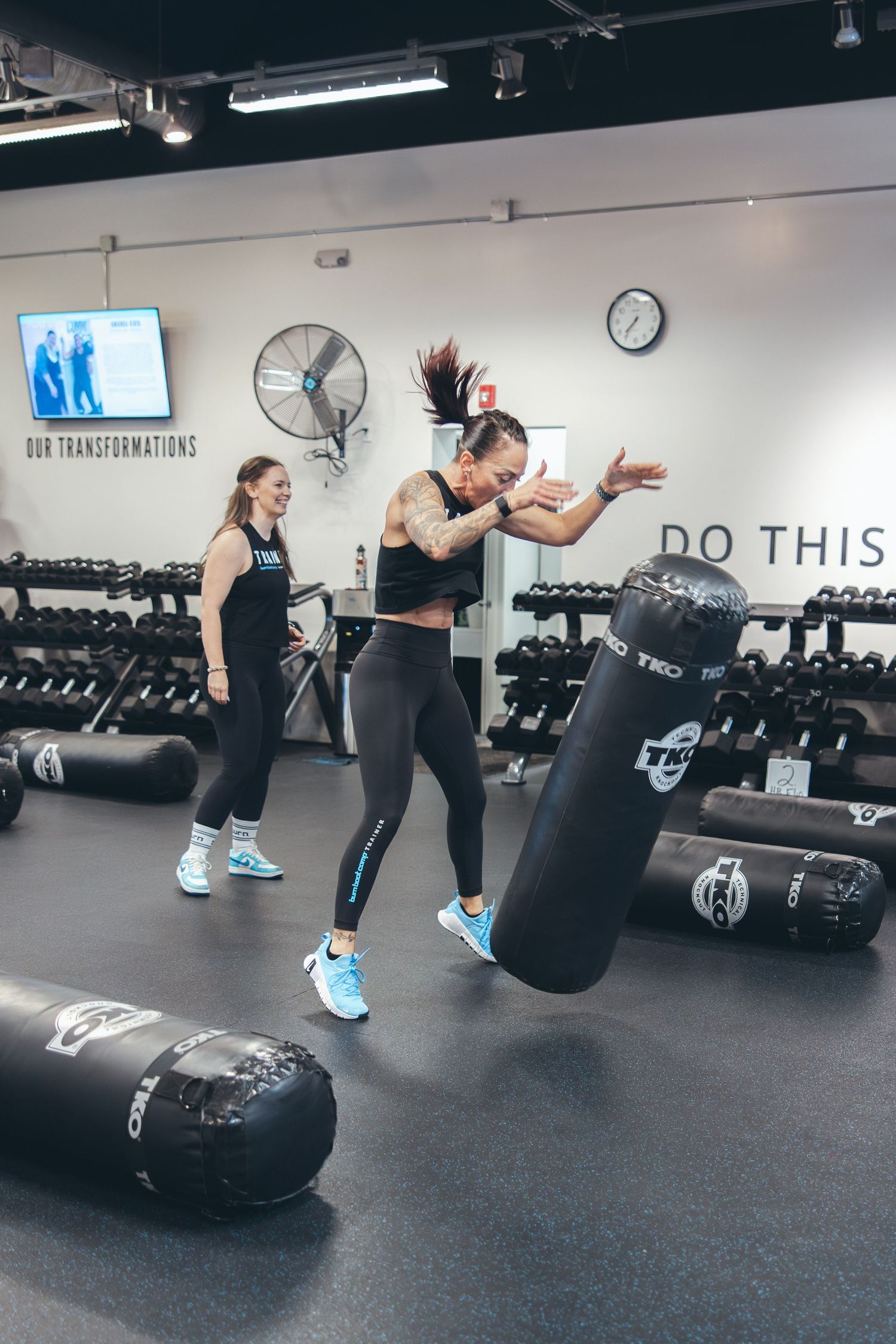 Athletes training with punching bags in modern fitness facility with white walls.