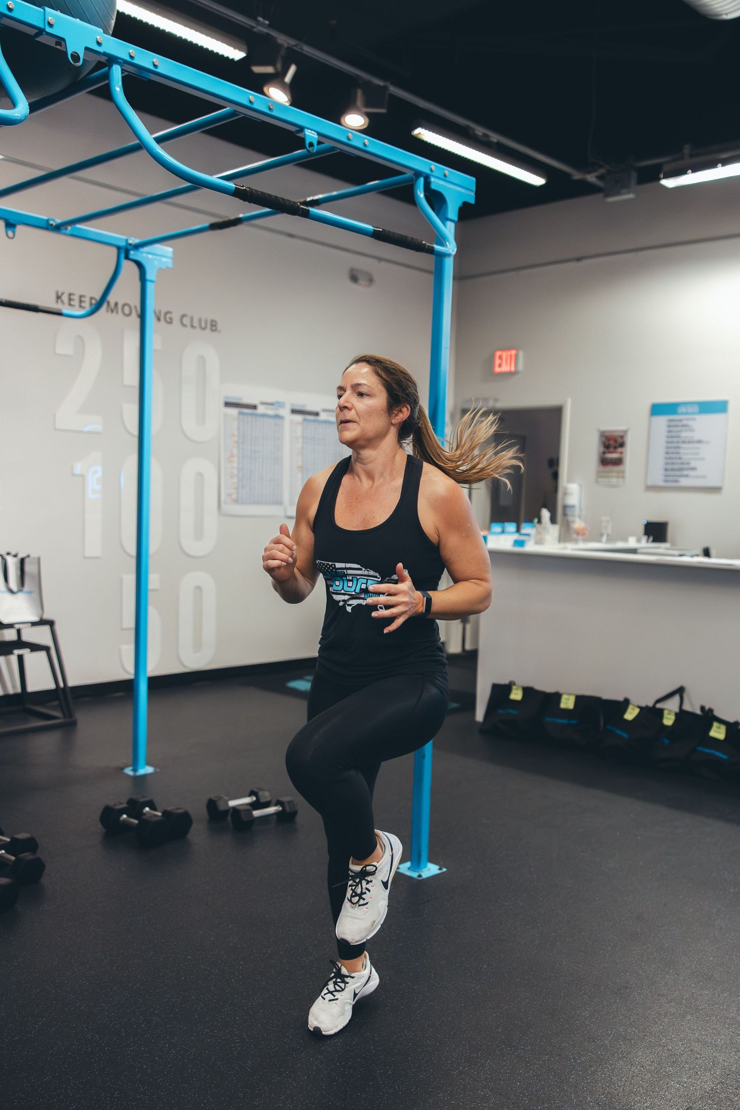 An athlete performs high knees exercise in a gym with blue equipment in the background.