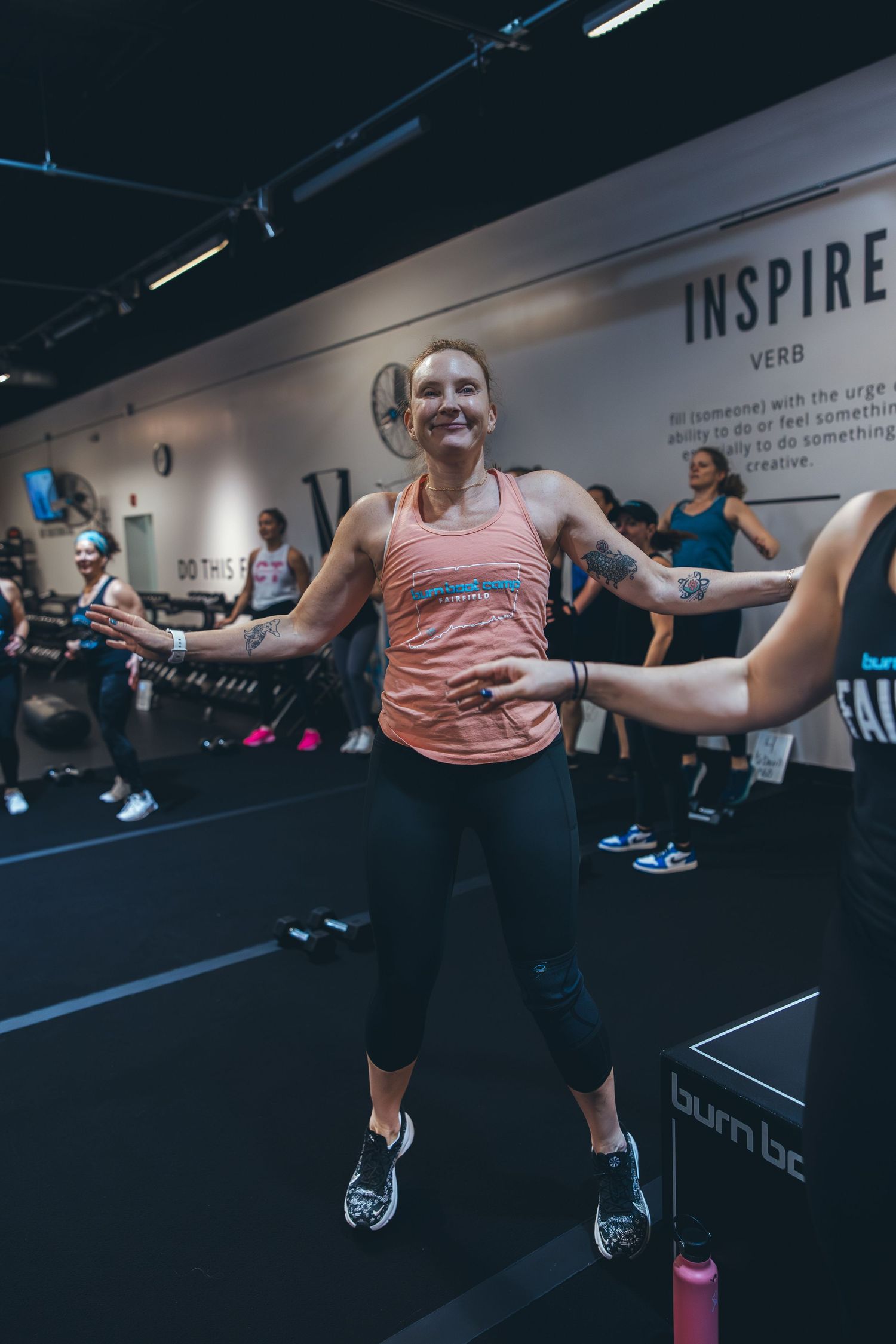 Fitness participant mid-jump during high-energy workout class in modern gym.