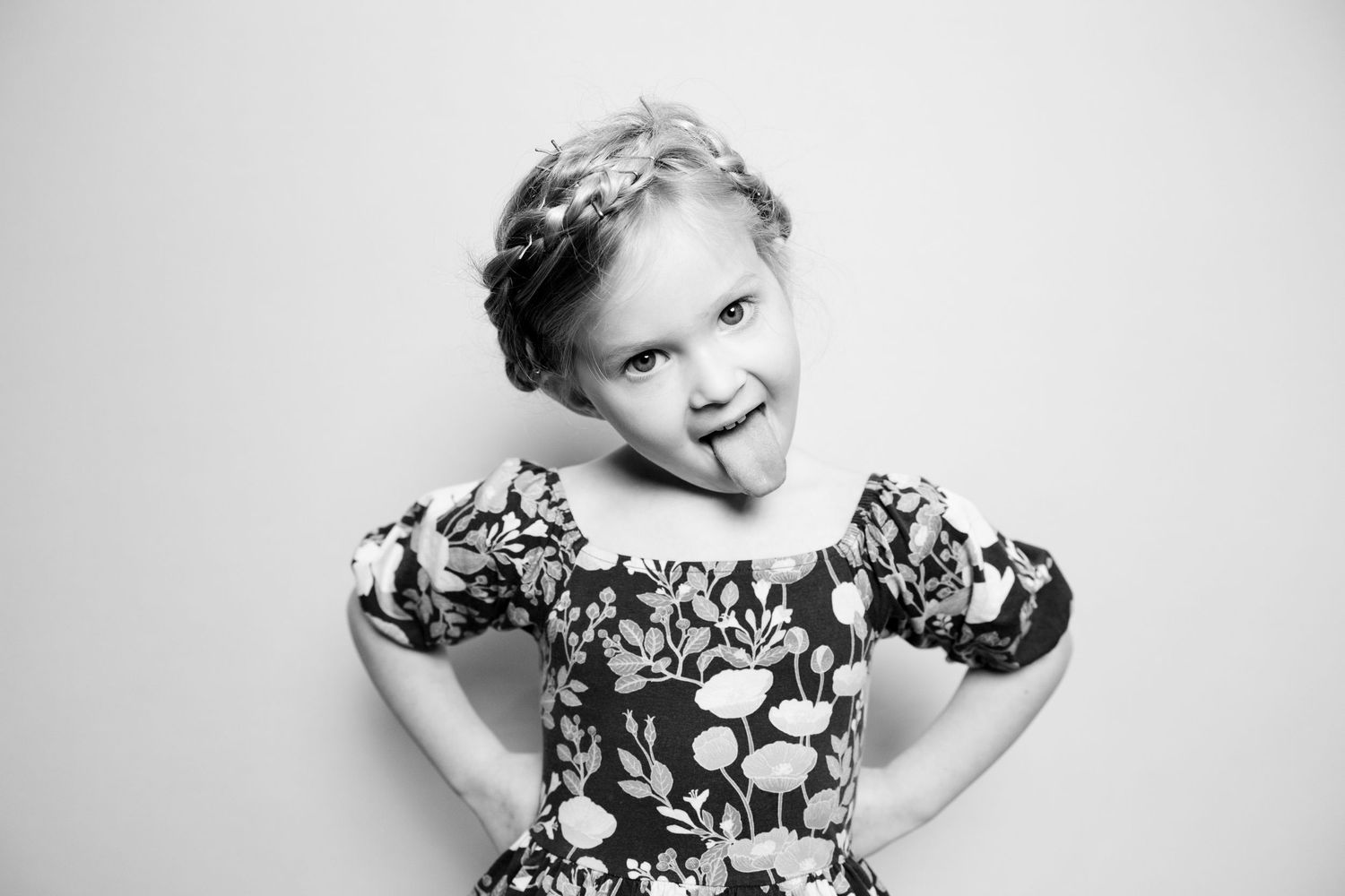 A young child in a black and white floral dress poses playfully in a series of expressive portraits against a light background.