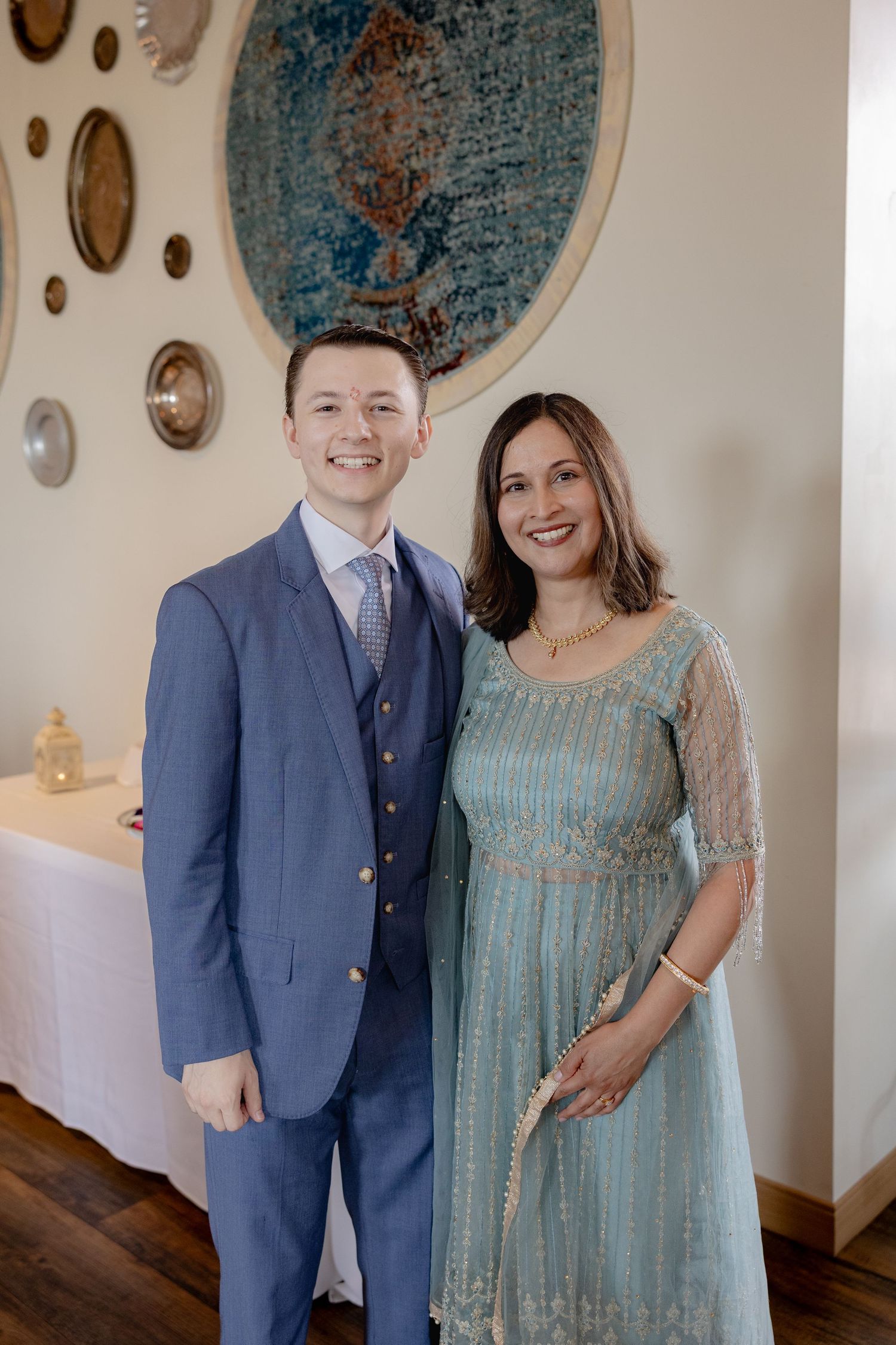 A couple in formal attire poses together against a light wall with decorative wall art.