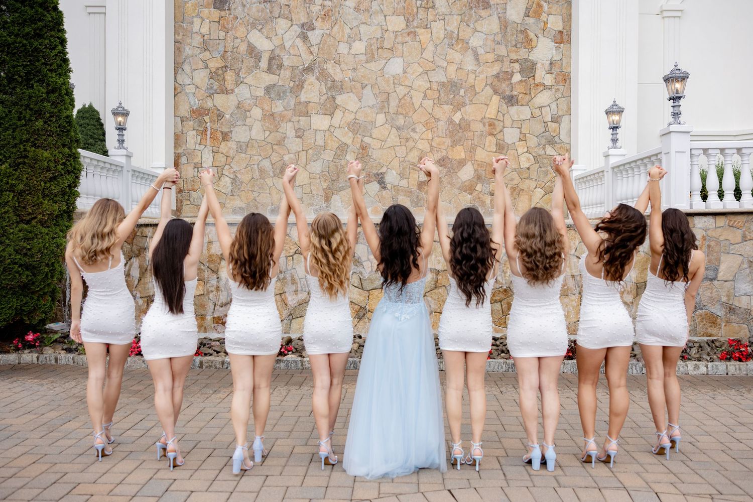 A group of women in white dresses and one in blue stand with their backs turned, showing off their long flowing hair.
