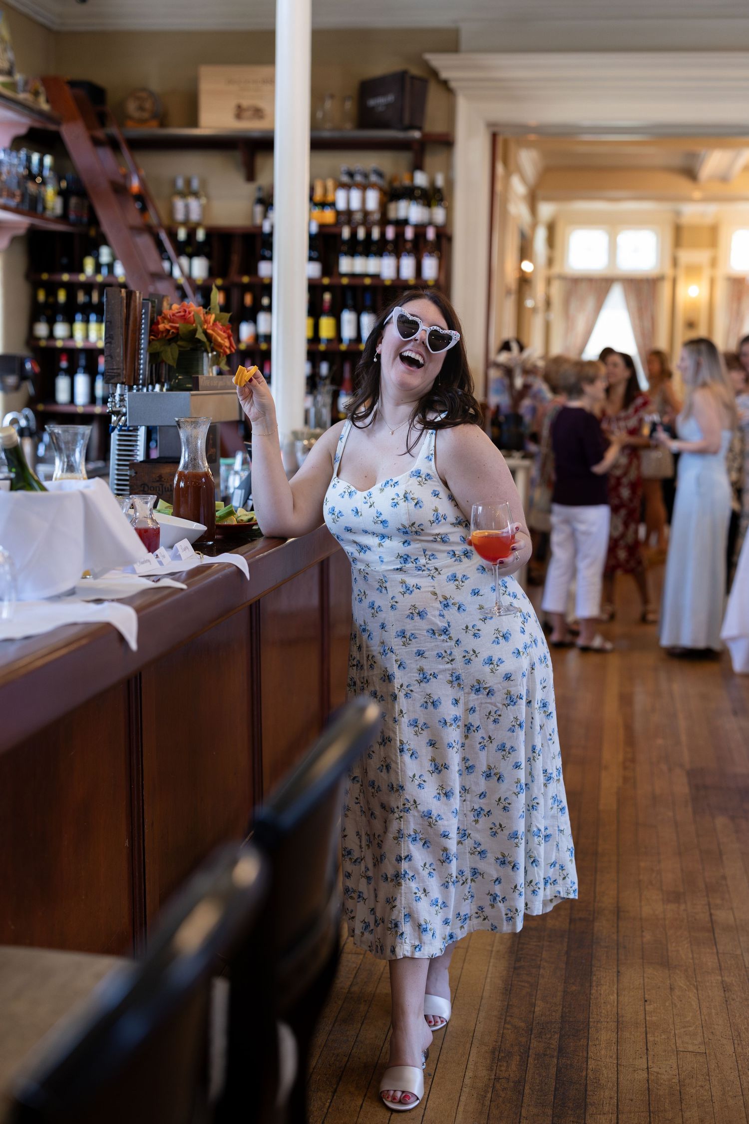 A sequence of five photos showing a person in a floral dress walking through a sunlit room with wooden floors and wine bottles.