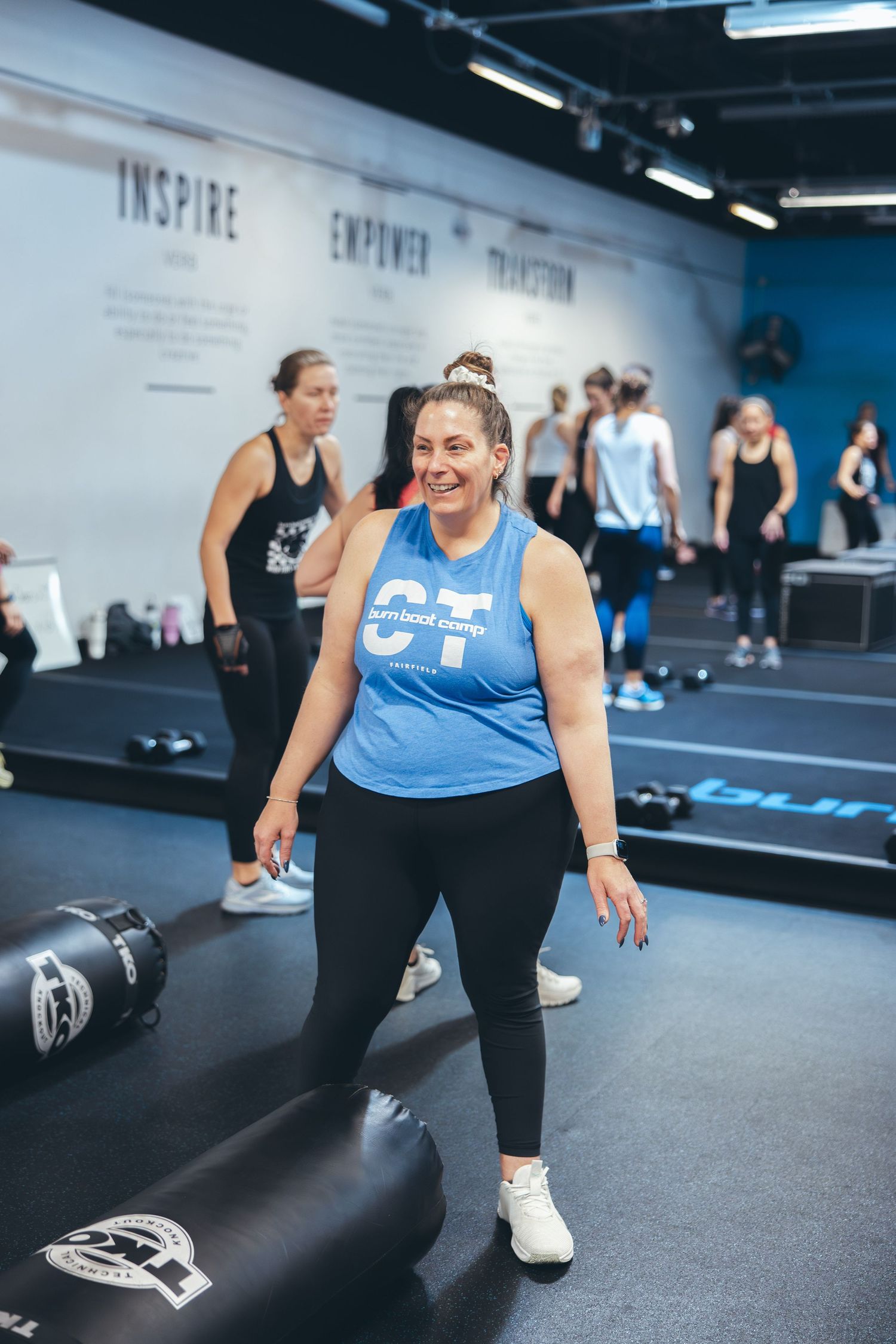 Fitness enthusiast smiling during workout session in modern gym with motivational wall text.