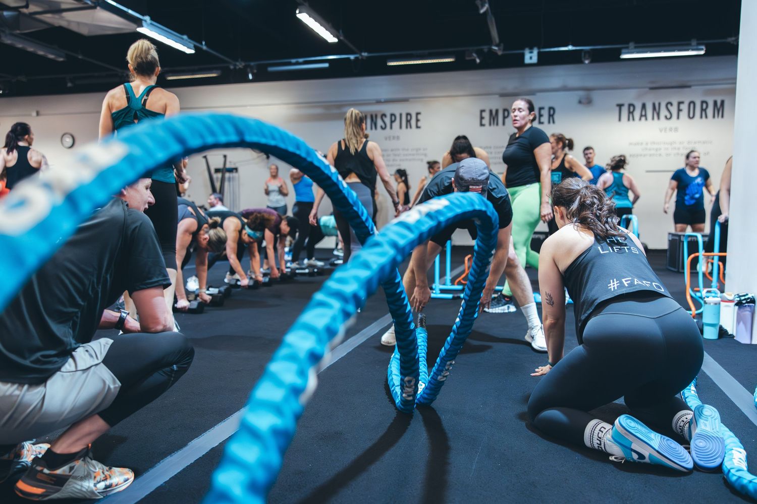 People performing exercises with bright blue battle ropes in a dynamic group fitness class.