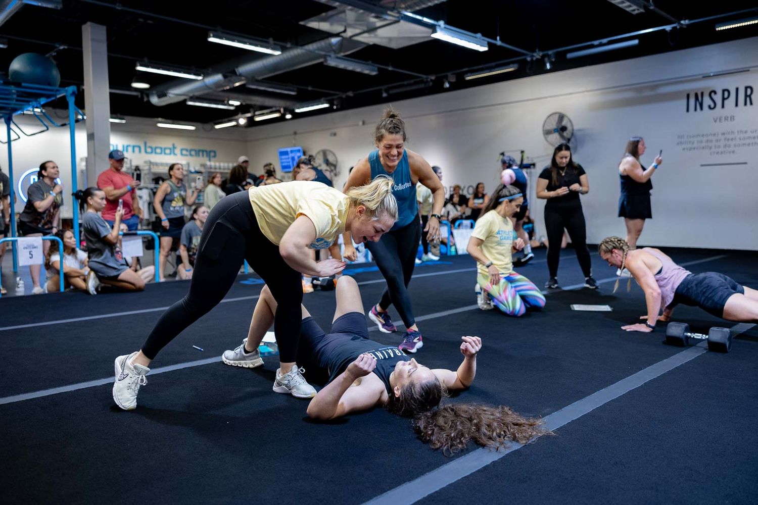 Group workout session in a modern gym with participants doing stretching and flexibility exercises on the floor.