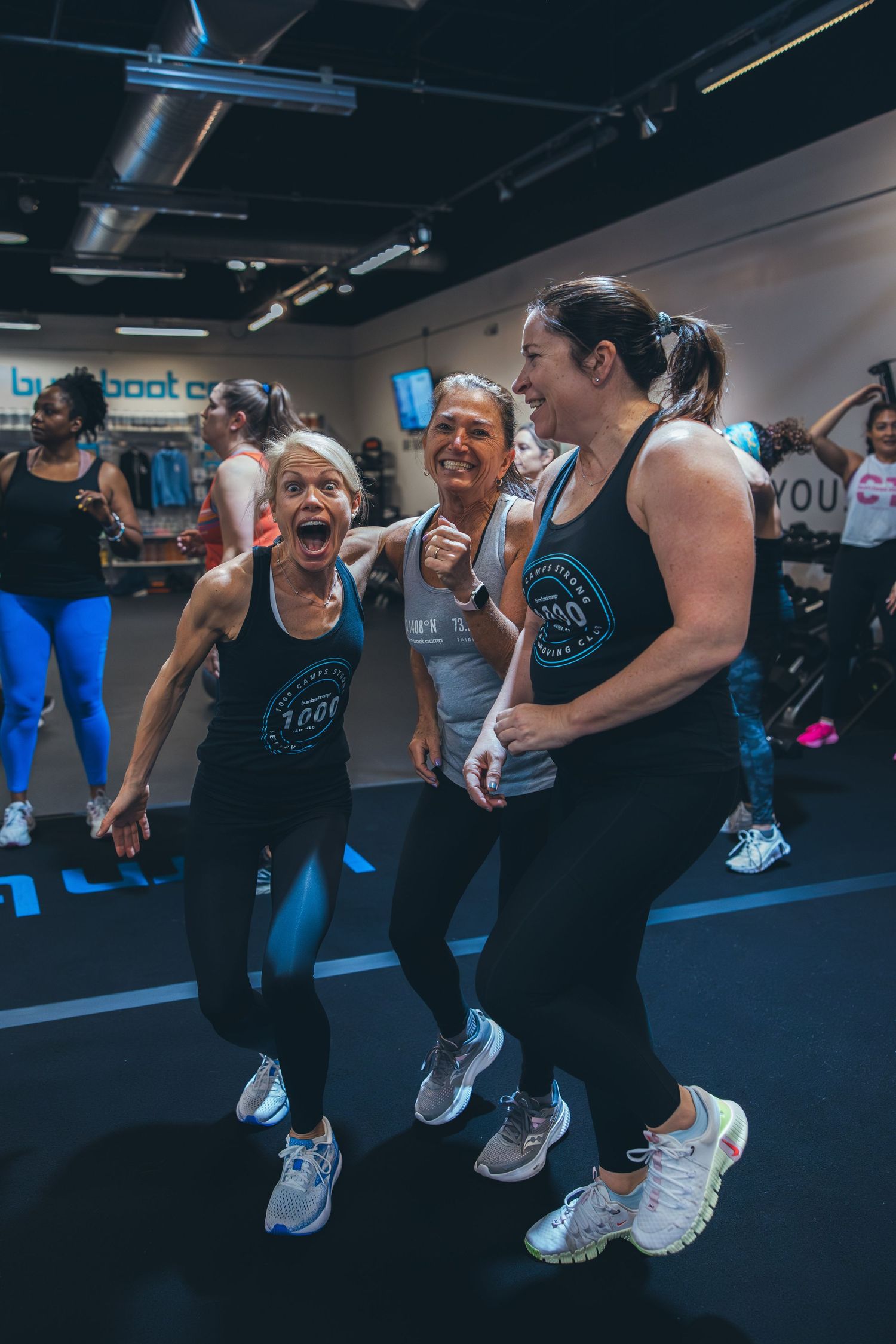 Participants jumping with excitement during group workout session in dark gym setting.